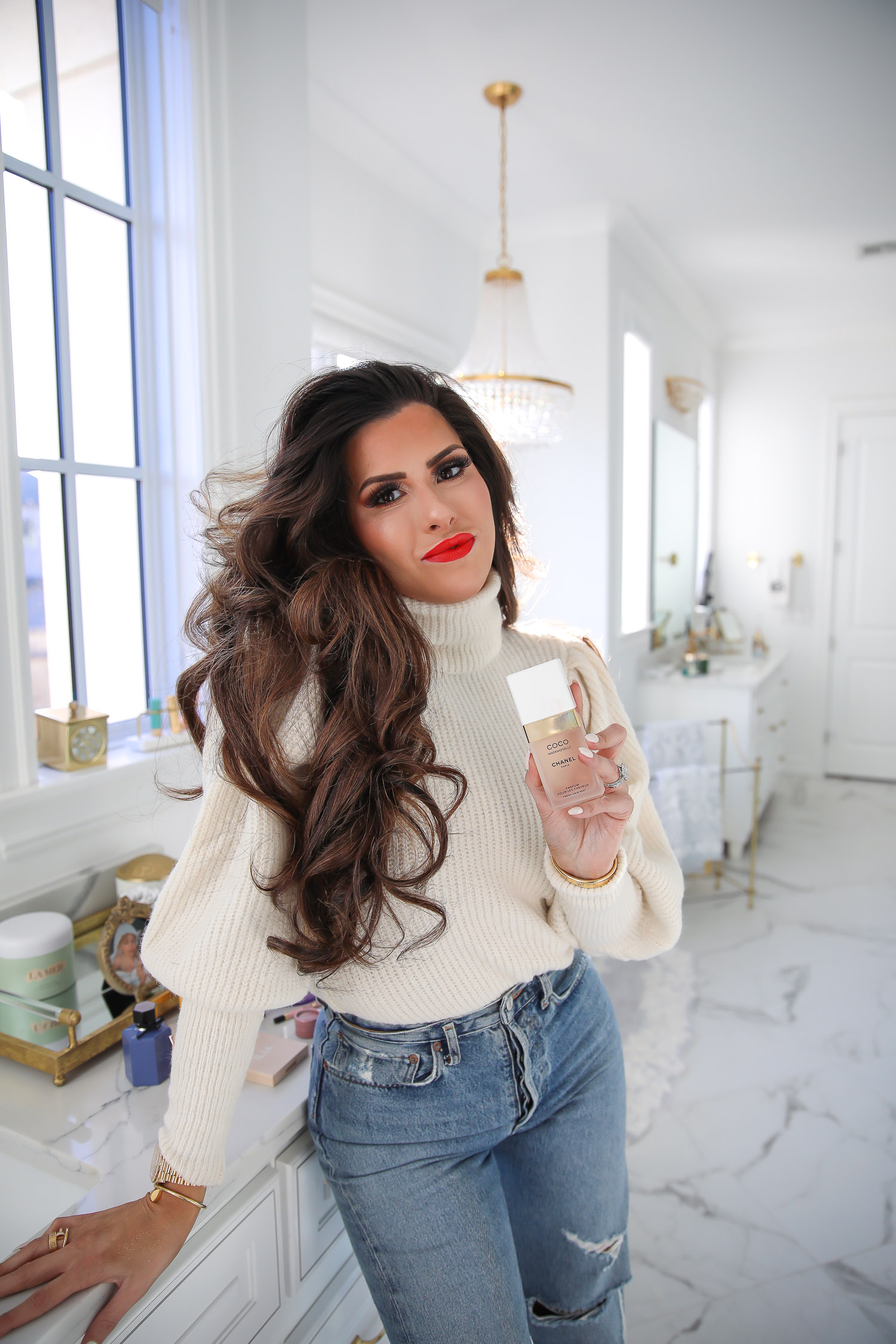 Chanel mademoiselle hair perfume review, Emily Gemma, beauty blogger |Sephora Favorites by popular US beauty blog, The Sweetest Thing: image of a woman wearing a cream turtleneck sweater, distressed denim and standing next to her bathroom vanity while holding Coco Chanel perfume. 