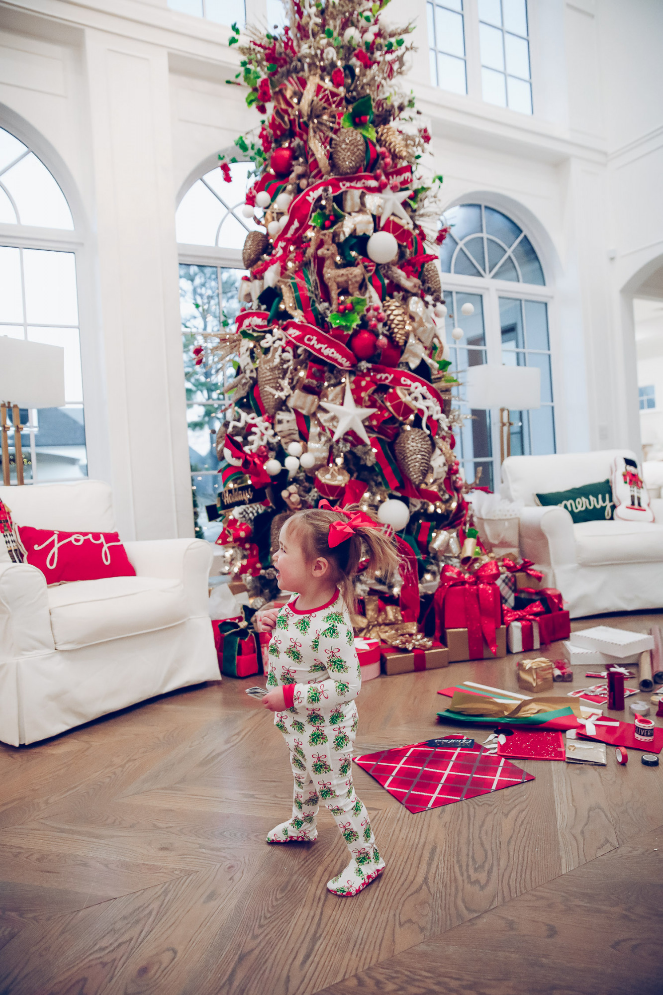 walmart gift wrap christmas 2020, shop hello holidays christmas tree, magnetic me PJs, emily ann gemma-10 | Gift Wrapping Ideas by popular US life and style blog, The Sweetest Thing: image of a little girl wearing Magnetic Me Christmas pjs while standing next to Christmas wrapping paper spread all over the floor in front of a Christmas tree with red, green and gold ornaments. 