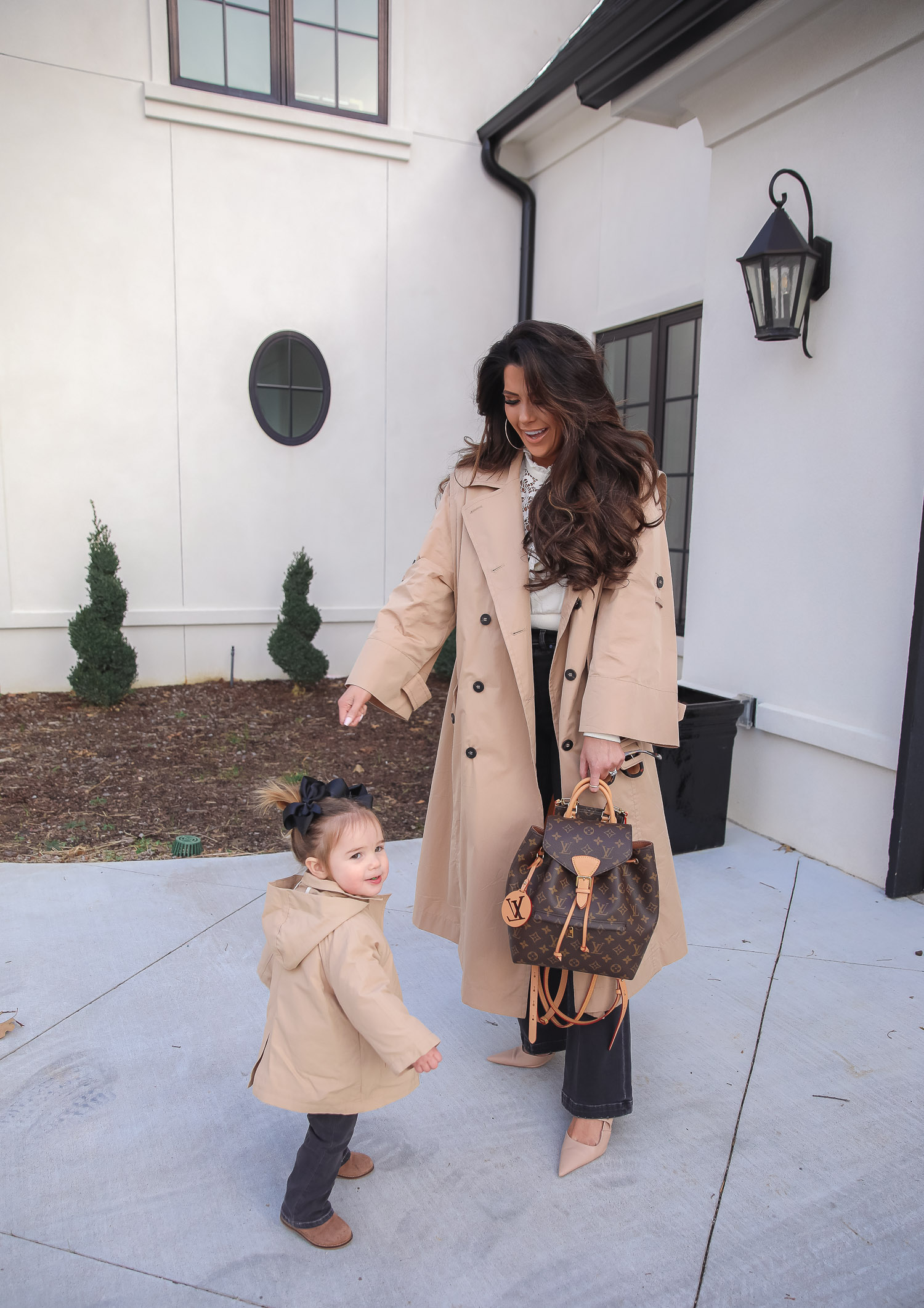 Express spring fashion 2021, emily gemma, mommy daughter matching outfits pinterest, baby fashion blogger, express trench coat 2021 |Mommy and Me Outfits by popular US fashion blog, The Sweetest Thing: image of Emily Gemma and her daughter Sophie standing outside and wearing a Express trench coat, Express flare jeans, Express gold hoop earrings, Express ruffle lack mock neck shirt, and holding a Louis Vuitton bags. 