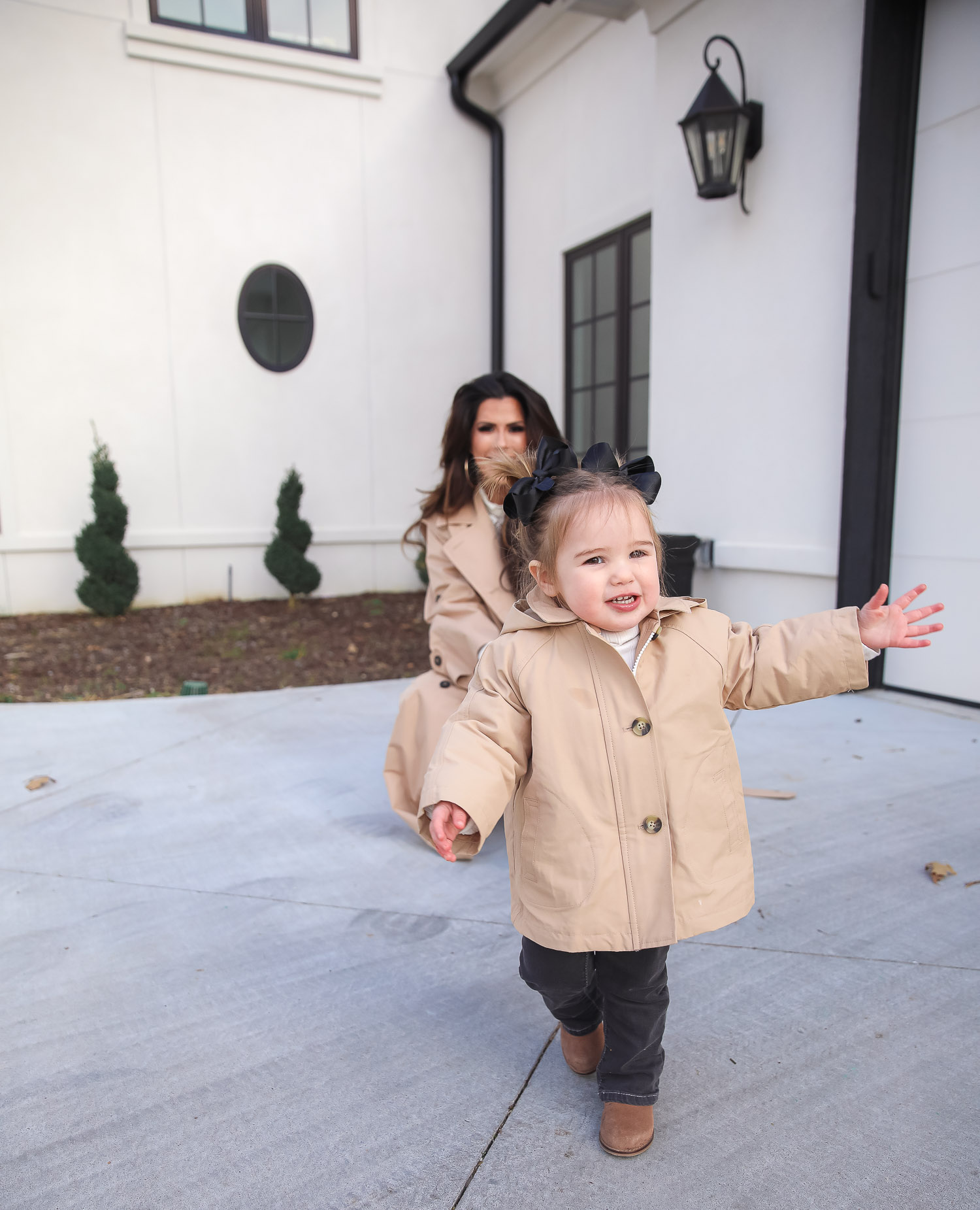 Express spring fashion 2021, emily gemma, mommy daughter matching outfits pinterest, baby fashion blogger, express trench coat 2021 |Mommy and Me Outfits by popular US fashion blog, The Sweetest Thing: image of Emily Gemma and her daughter Sophie standing outside and wearing a Express trench coat, Express flare jeans, Express gold hoop earrings, Express ruffle lack mock neck shirt, and holding a Louis Vuitton bags. 