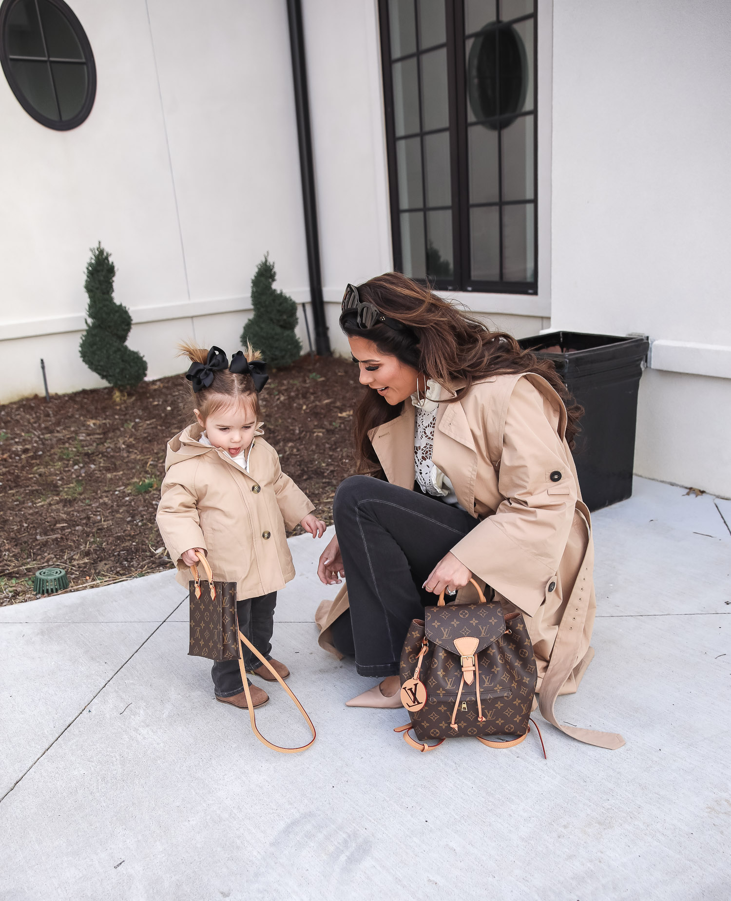 Express spring fashion 2021, emily gemma, mommy daughter matching outfits pinterest, baby fashion blogger, express trench coat 2021 |Mommy and Me Outfits by popular US fashion blog, The Sweetest Thing: image of Emily Gemma and her daughter Sophie standing outside and wearing a Express trench coat, Express flare jeans, Express gold hoop earrings, Express ruffle lack mock neck shirt, and holding a Louis Vuitton bags. 