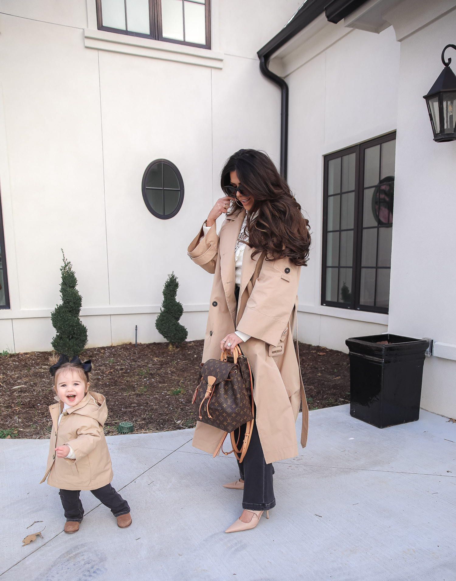 Express spring fashion 2021, emily gemma, mommy daughter matching outfits pinterest, baby fashion blogger, express trench coat 2021 |Mommy and Me Outfits by popular US fashion blog, The Sweetest Thing: image of Emily Gemma and her daughter Sophie standing outside and wearing a Express trench coat, Express flare jeans, Express gold hoop earrings, Express ruffle lack mock neck shirt, and holding a Louis Vuitton bags. 