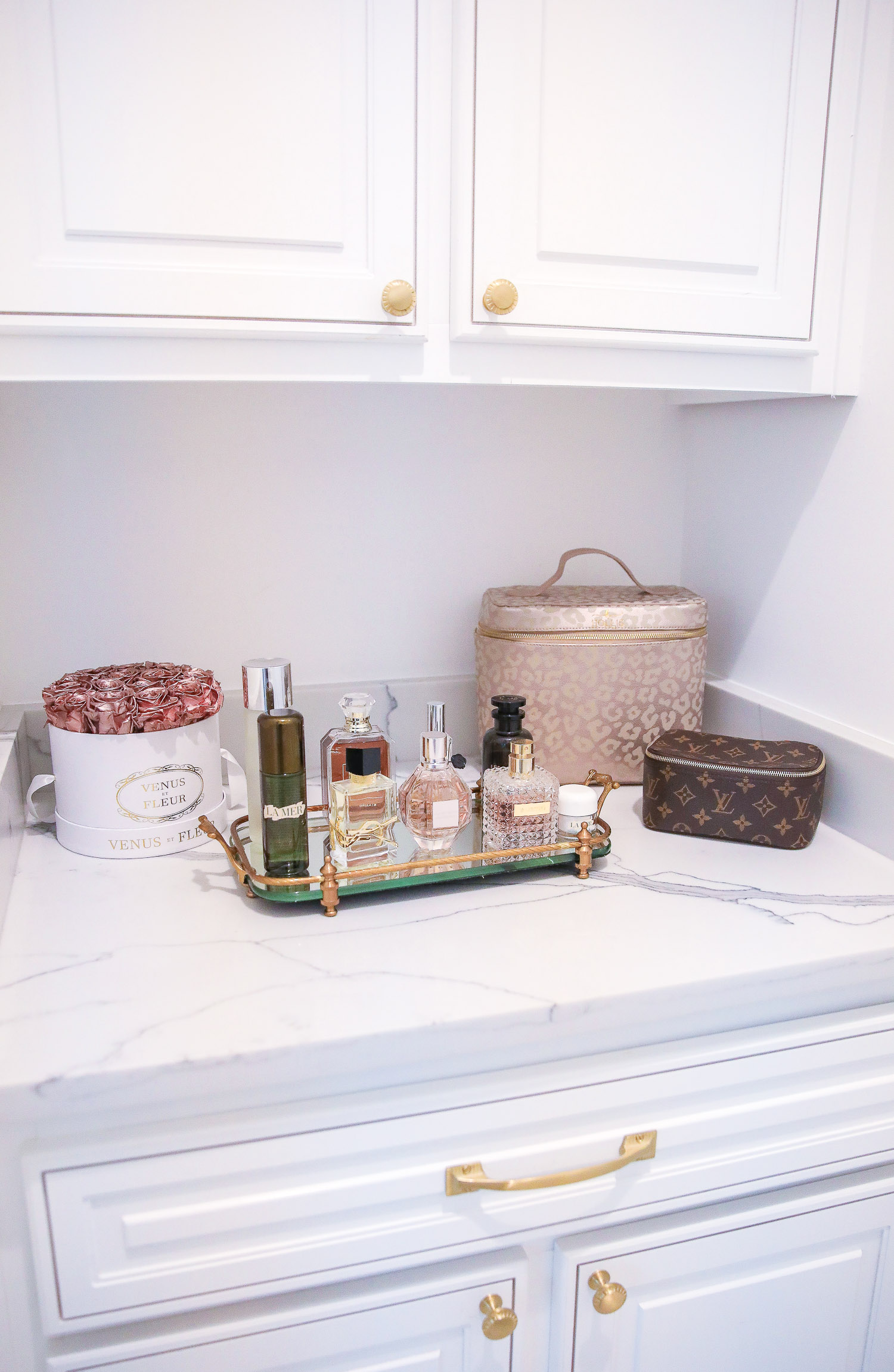 Top Picks by popular US life and style blog, The Sweetest Thing: image of a glass and gold metal tray filled with high end perfume bottles and resting on a white marble counter top next to a Louis Vuitton bag. 