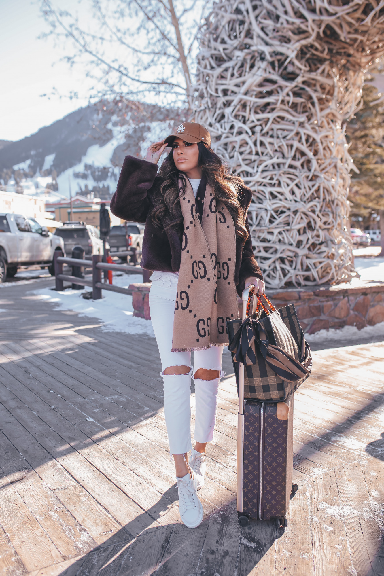 winter fashion outfit ideas, gucci jacquAed wool silk scarf, LA carharrt cap, Jackson hole fashion blog |Winter Fashion by popular US fashion blog, The Sweetest Thing: image of Emily Gemma standing by the antler arch in Jackson Hole, WY and wearing a Free People top, BB Dakota faux fur jacket, distressed white denim jeans, Gucci scarf, '47 brand cap, Le Specs sunglasses, and standing next to a Louis Vuitton rolling suitcase and holding a Fendi tote bag. 