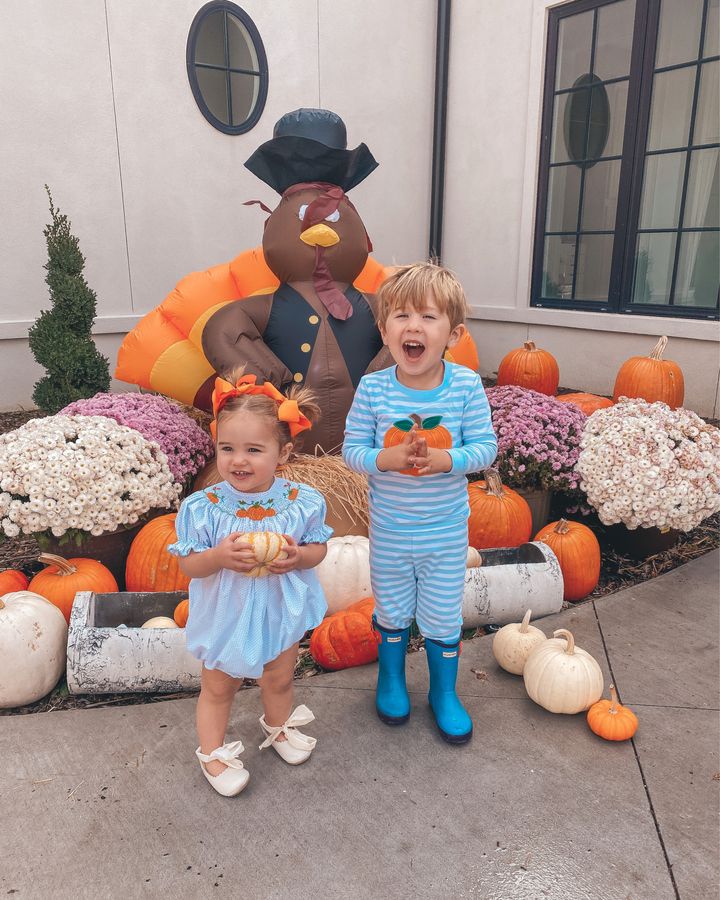 November Instagram Recap by popular US lifestyle blog, The Sweetest Thing: image of a young girl and a young boy standing in front of an inflatable turkey, potted mums, and orange and white pumpkins and wearing a blue romper, orange hair bows, cream bow tie shoes, blue and white stripe pumpkin pajamas, and blue hunter boots. 