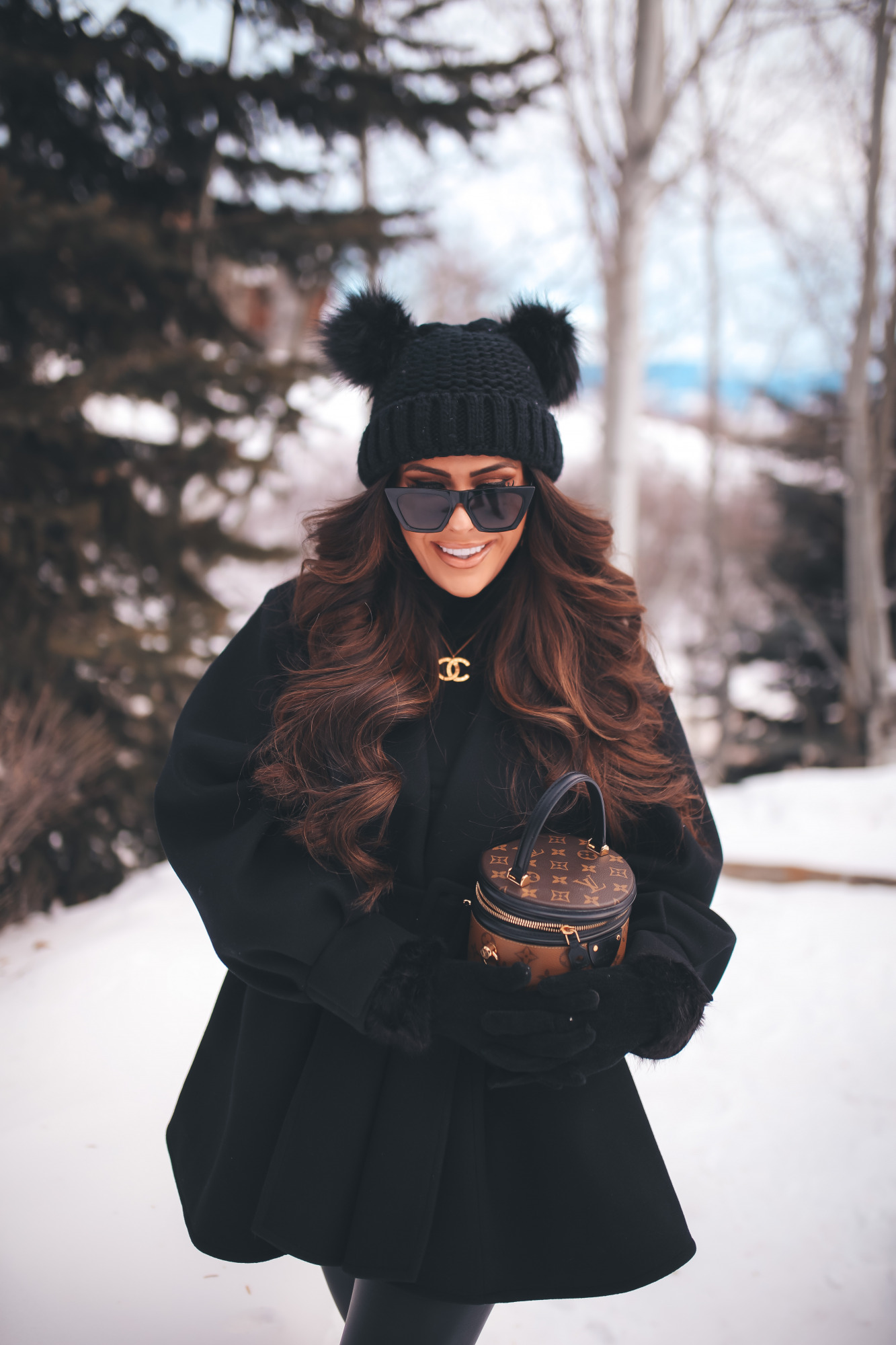 hair by chrissy extensions brunette balayage, louis vuitton cannes, jackson hole four seasons4 |Dressing Up by popular US fashion blog, The Sweetest Thing: image of Emily Gemma standing outside in the snow and wearing a Good American bodysuit, commando leggings, Chanel boots, Amazon sunglasses, Storets puff sleeve coat, Tasha double pom beanie, and holding a Louis Vuitton bag. 