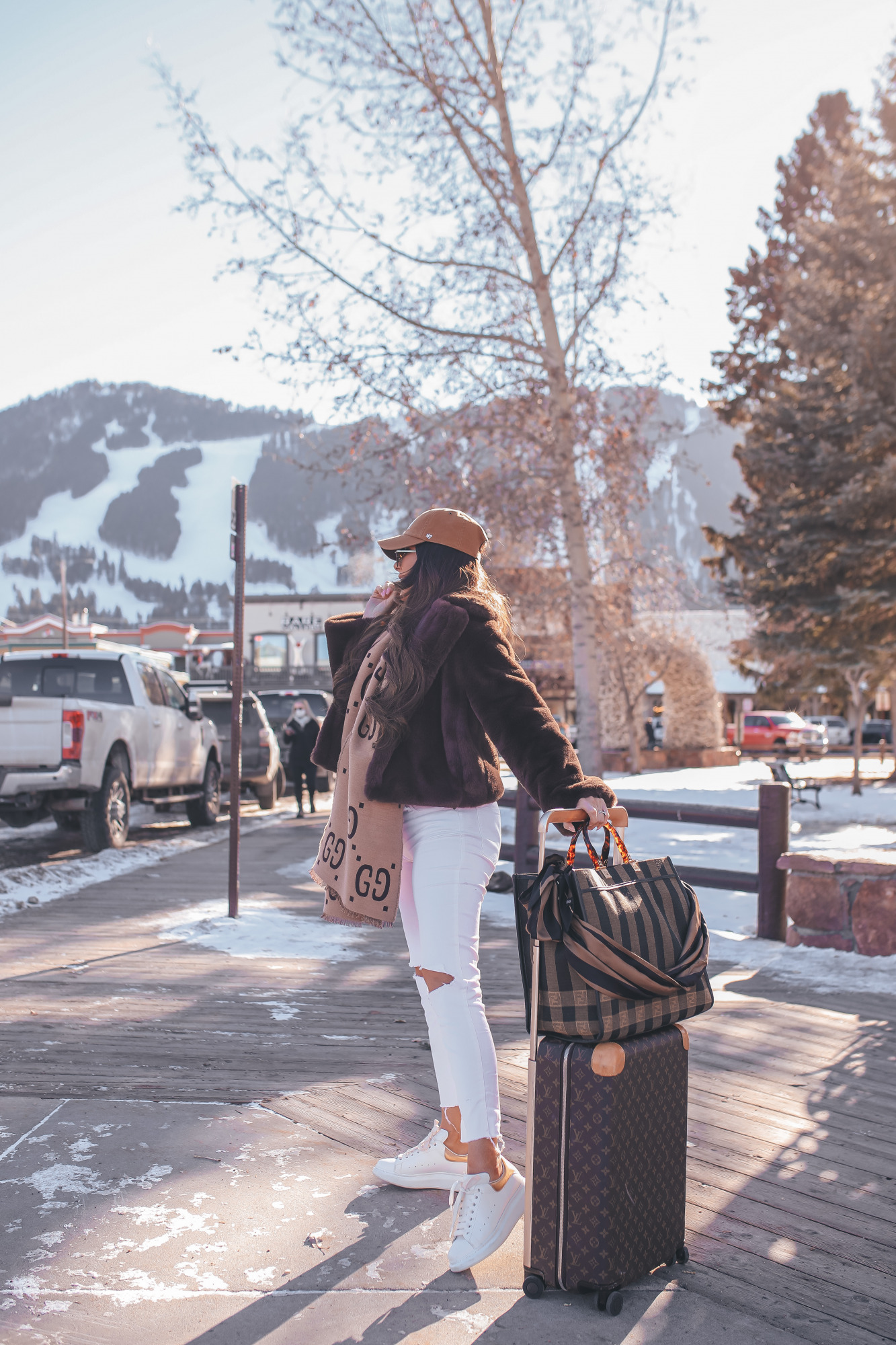 winter fashion outfit idea pinterest 2021, white denim in winter, louis vuitton horizon 55 carry on |Winter Fashion by popular US fashion blog, The Sweetest Thing: image of Emily Gemma standing outside in downtown Jackson Hole, WY and wearing a Free People top, BB Dakota faux fur jacket, distressed white denim jeans, Gucci scarf, '47 brand cap, Le Specs sunglasses, and standing next to a Louis Vuitton rolling suitcase and holding a Fendi tote bag.