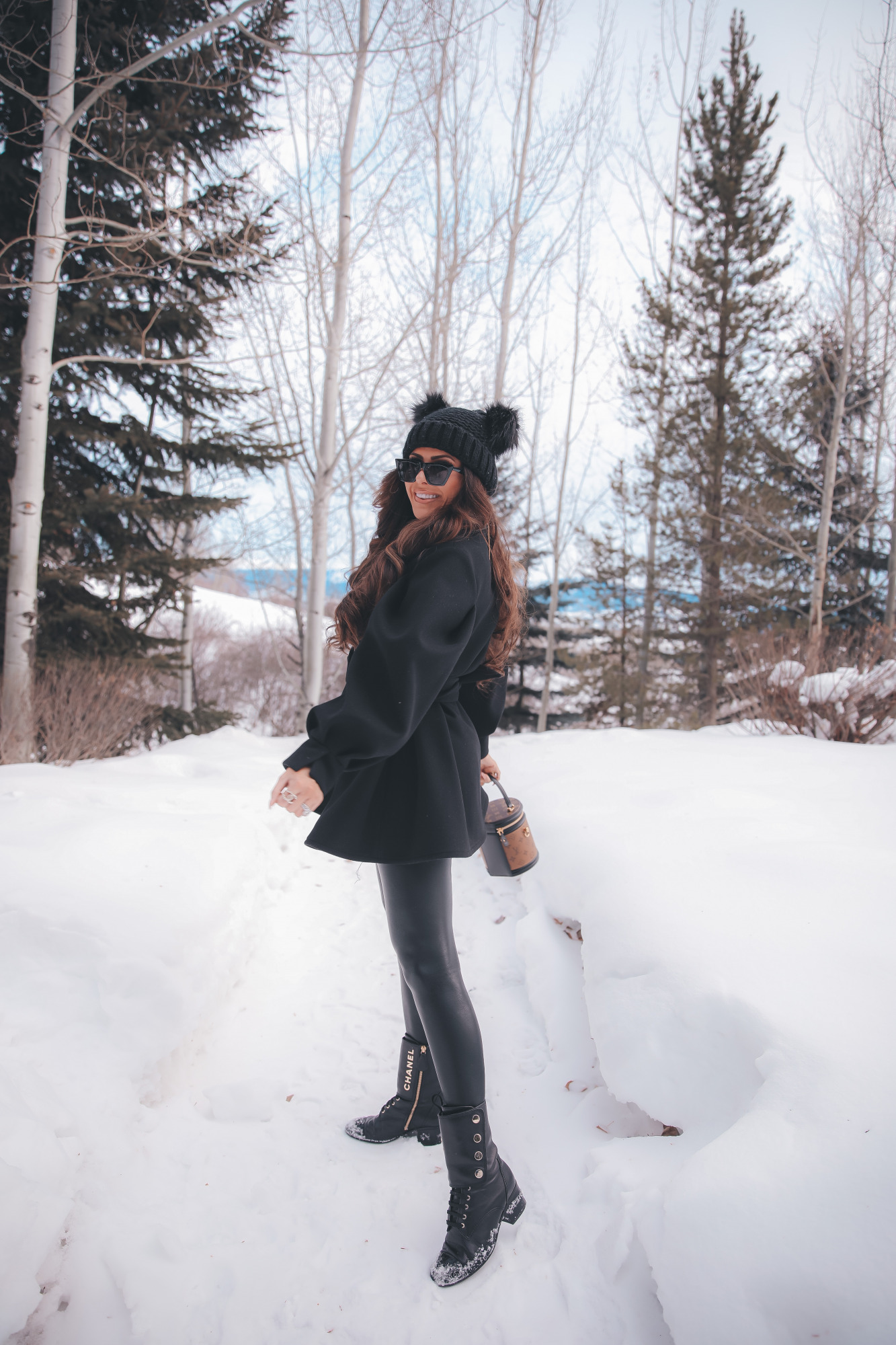 louis vuitton cannes bag, amazon cat eye sunglasses, pinterest winter fashion outfit ideas, emily gemma |Dressing Up by popular US fashion blog, The Sweetest Thing: image of Emily Gemma standing outside in the snow and wearing a Good American bodysuit, commando leggings, Chanel boots, Amazon sunglasses, Storets puff sleeve coat, Tasha double pom beanie, and holding a Louis Vuitton bag. 