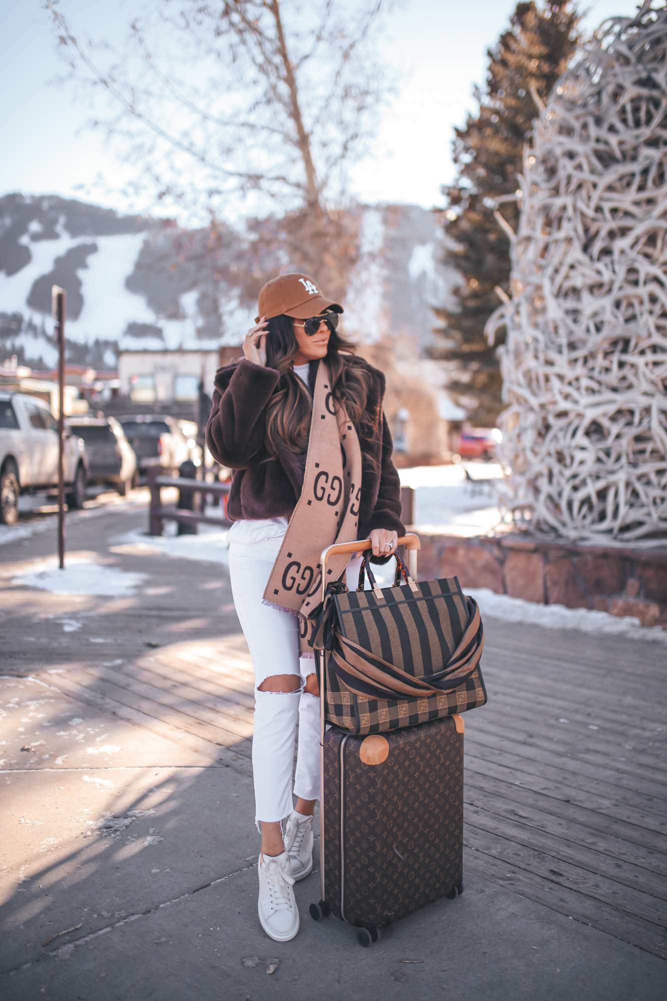 winter fashion outfit idea pinterest 2021, white denim in winter, louis vuitton horizon 55 carry on |Winter Fashion by popular US fashion blog, The Sweetest Thing: image of Emily Gemma standing outside in downtown Jackson Hole, WY and wearing a Free People top, BB Dakota faux fur jacket, distressed white denim jeans, Gucci scarf, '47 brand cap, Le Specs sunglasses, and standing next to a Louis Vuitton rolling suitcase and holding a Fendi tote bag. 
