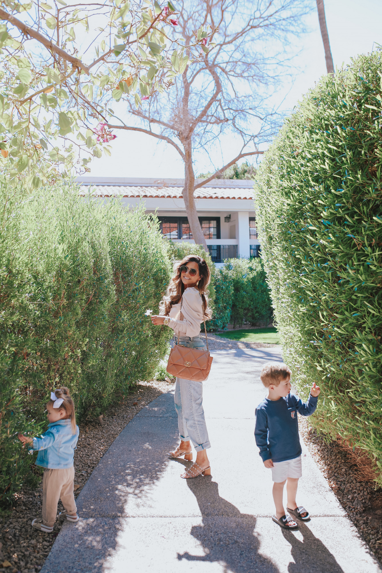 high waisted mom jeans 2021 trend outfit idea pinterest, chanel caramel 19 medium, scottsdale fashion blog, emily gemma |Mom Jeans by popular US fashion blog, The Sweetest Thing: image of Emily Gemma at standing outside in Scottsdale, Arizona and wearing Slvrlake mom jeans, Astr the Label top, gold Rolex watch, Cartier rings, Chanel purse, cartier bracelets, and Chanel necklace and walking with her kids while they wear a Vineyard Vines t-shirt, tan shorts, Nike slide sandals, white hair bows, jean jacket, white t-shirt, and tan pants. 