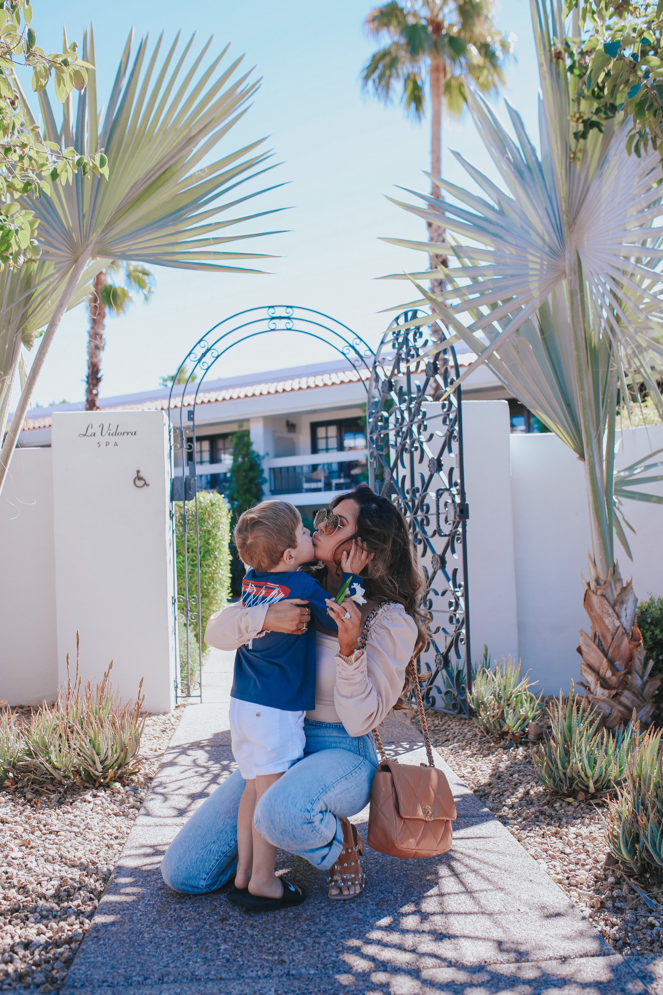 high waisted mom jeans 2021 trend outfit idea pinterest, chanel caramel 19 medium, scottsdale fashion blog, emily gemma4 |Mom Jeans by popular US fashion blog, The Sweetest Thing: image of Emily Gemma at standing outside in Scottsdale, Arizona and wearing Slvrlake mom jeans, Astr the Label top, gold Rolex watch, Cartier rings, Chanel purse, cartier bracelets, and Chanel necklace and kissing her son on the lips while he's wearing a Vineyard Vines t-shirt and tan shorts. 