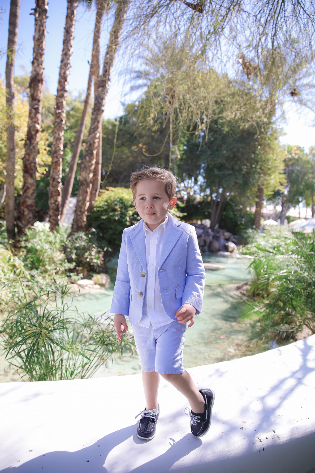 janie and jack easter kids outfits 2021, kids easter outfit ideas toddler, emily gemma, scottsdale fashion blog4 |Spring Outfit Ideas for Kids by popular US fashion blog, The Sweetest Thing: image of a young boy standing outside next to a landscaped pond and wearing a Seersucker Blazer, Seersucker Shorts, White Button-down, and Leather Boat Shoes.