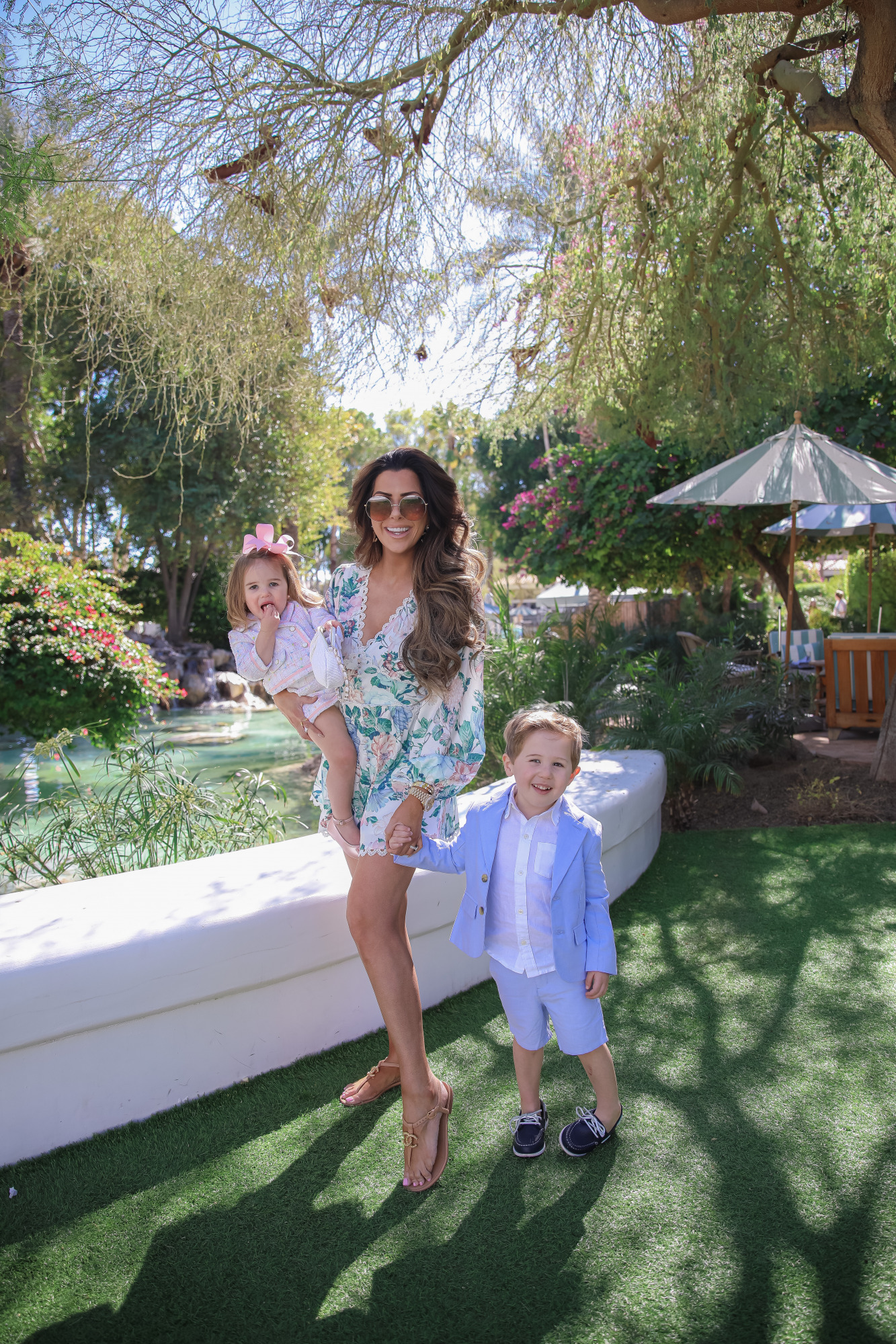 little girls easter outfit ideas, baby girl fashion blogger outfit idea pinterest, Emily Gemma | Spring Outfit Ideas for Kids by popular US fashion blog, The Sweetest Thing: image of Emily Gemma standing outside with her two kids by a landscaped pond and wearing a Pink Boucle Jacket, Pink Boucle Shorts, Pink Bow Flats, White Purse, Straw Sun Hat, Seersucker Blazer, Seersucker Shorts, White Button-down, and Leather Boat Shoes.