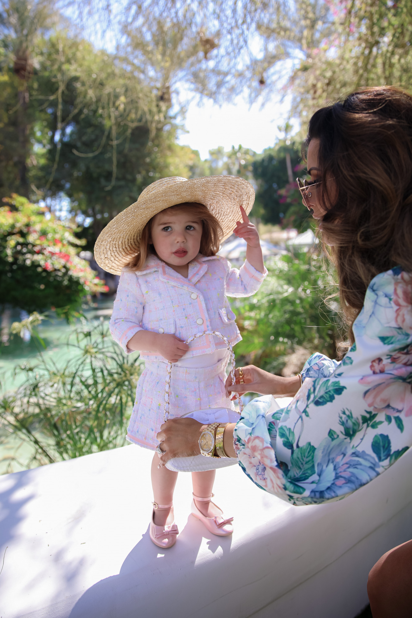 janie and jack easter kids outfits 2021, kids easter outfit ideas toddler, emily gemma, scottsdale fashion blog4 |Spring Outfit Ideas for Kids by popular US fashion blog, The Sweetest Thing: image of a young girl standing outside next to a landscaped pond and wearing a Pink Boucle Jacket, Pink Boucle Shorts, Pink Bow Flats, White Purse, and Straw Sun Hat.