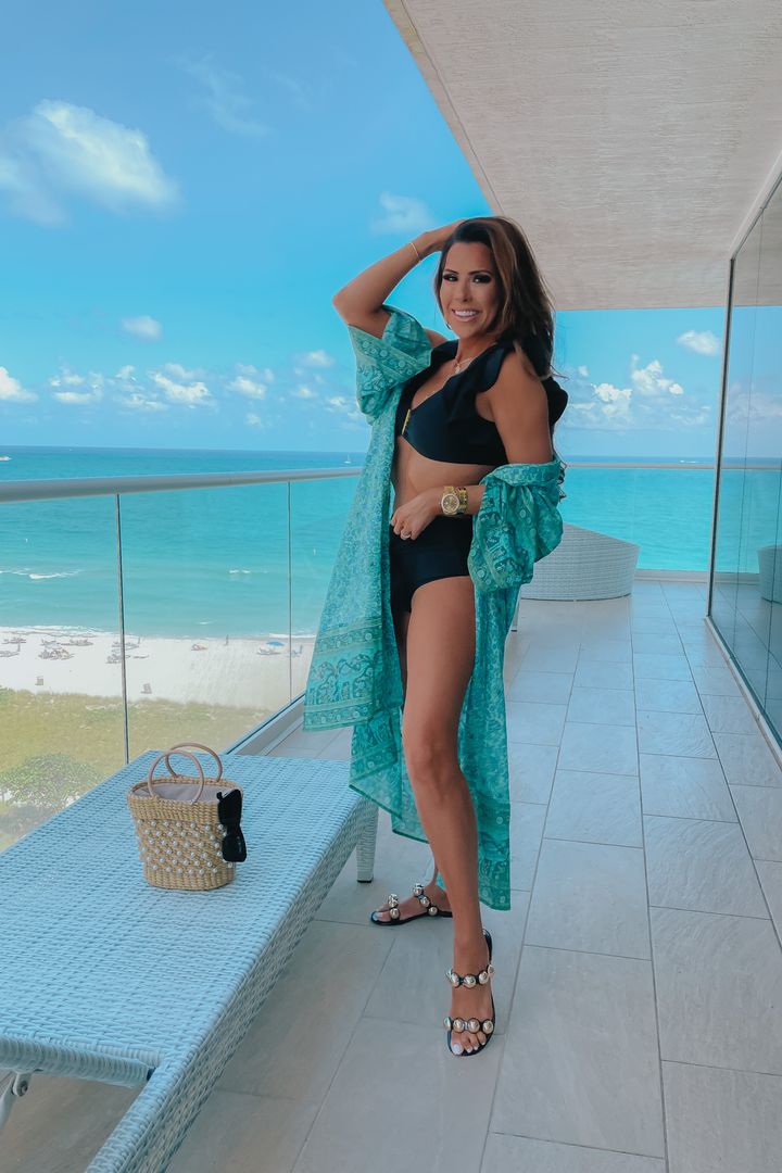 Beach Oufit, Beach Bag, Best Summer Sandals, Best Swimsuits Summer 2021, Beach Outfit Inspiration, Emily Ann Gemma |Instagram Recap by popular US fashion blog, The Sweetest Thing: image of Emily Gemma standing on a balcony and wearing a black two piece swimsuit and teal coverup with black studded strap slide sandals. 