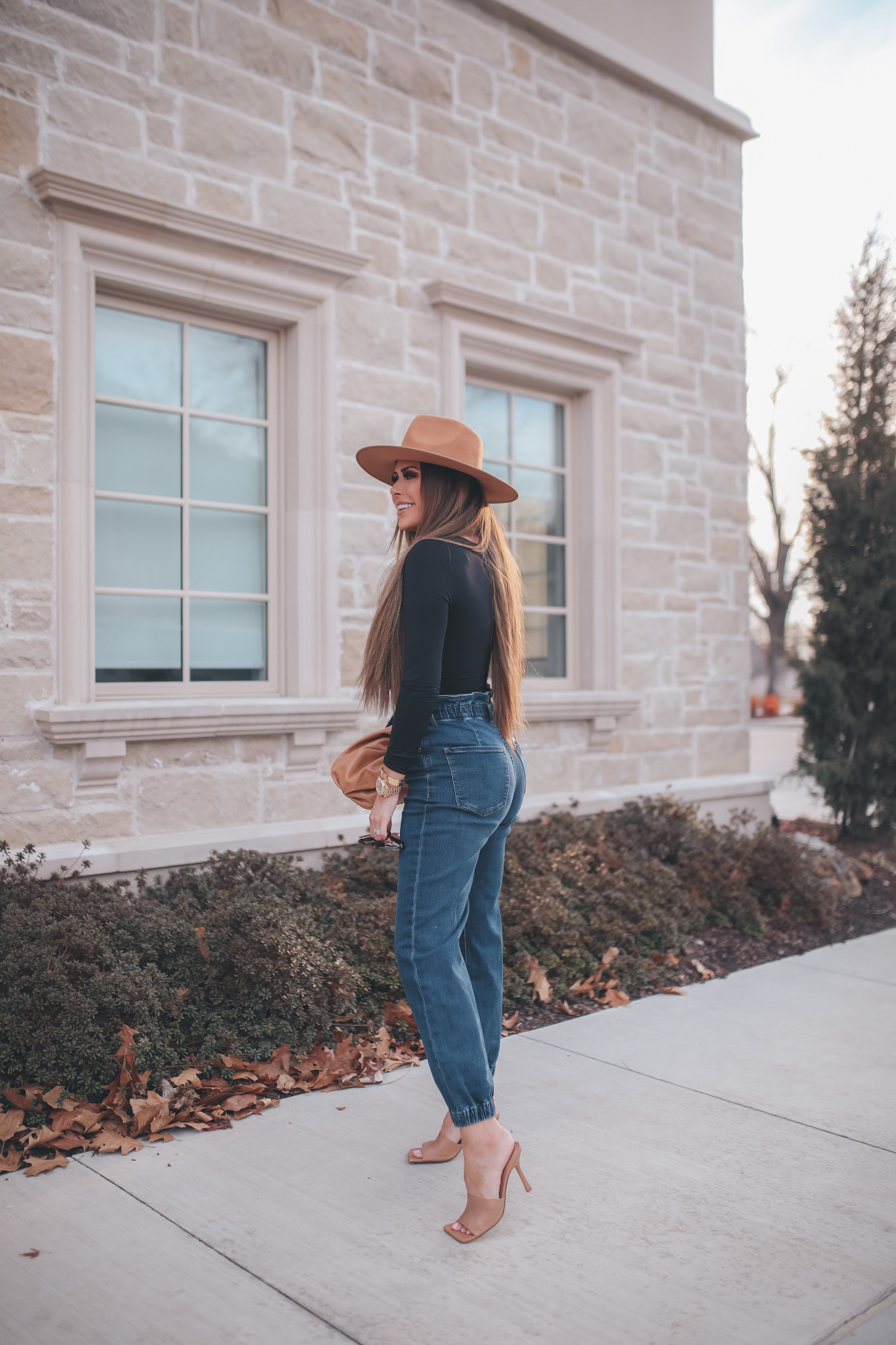 express spring fashion 2021, bottega clutch dupe, denim high waisted joggers, emily gemma15 |Body Contour by popular US fashion blog, The Sweetest Thing: image of a Emily Gemma wearing an Express black bodysuit, Express high waisted joggers, tan heel slide sandals, tan felt fedora, and holding a Bottega clutch dupe.