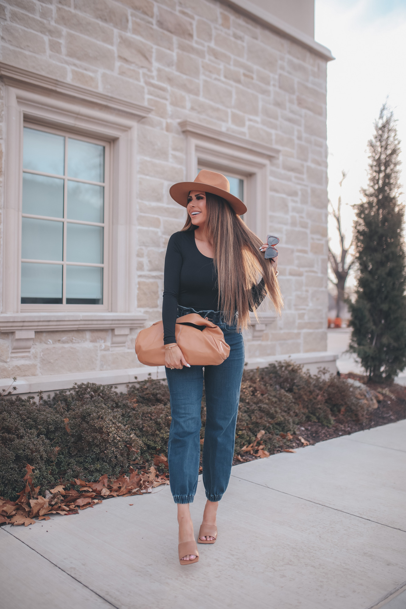 express spring fashion 2021, bottega clutch dupe, denim high waisted joggers, emily gemma15 |Body Contour by popular US fashion blog, The Sweetest Thing: image of a Emily Gemma wearing an Express black bodysuit, Express high waisted joggers, tan heel slide sandals, tan felt fedora, and holding a Bottega clutch dupe.