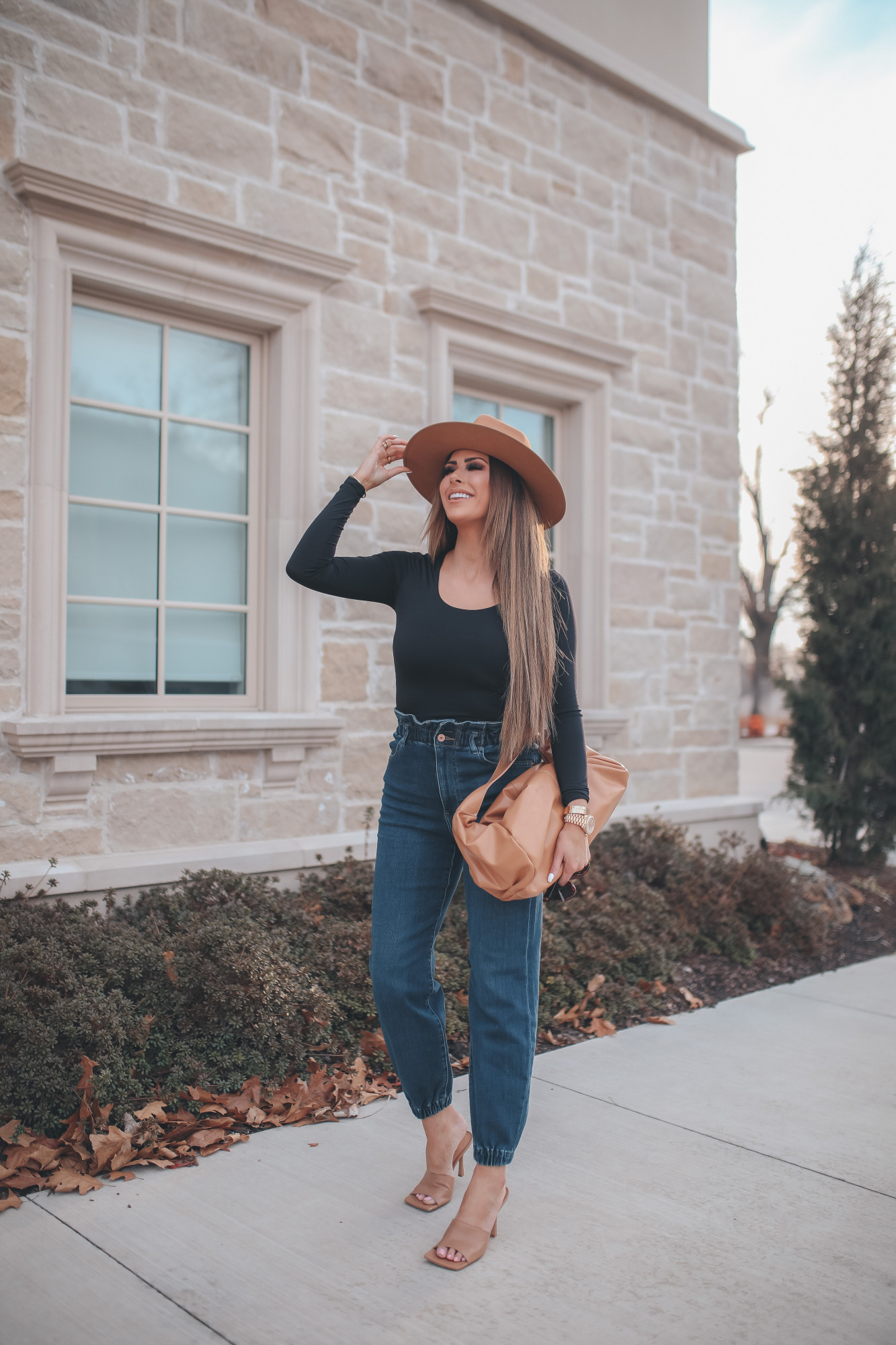 express spring fashion 2021, bottega clutch dupe, denim high waisted joggers, emily gemma15 |Body Contour by popular US fashion blog, The Sweetest Thing: image of a Emily Gemma wearing an Express black bodysuit, Express high waisted joggers, tan heel slide sandals, tan felt fedora, and holding a Bottega clutch dupe. 