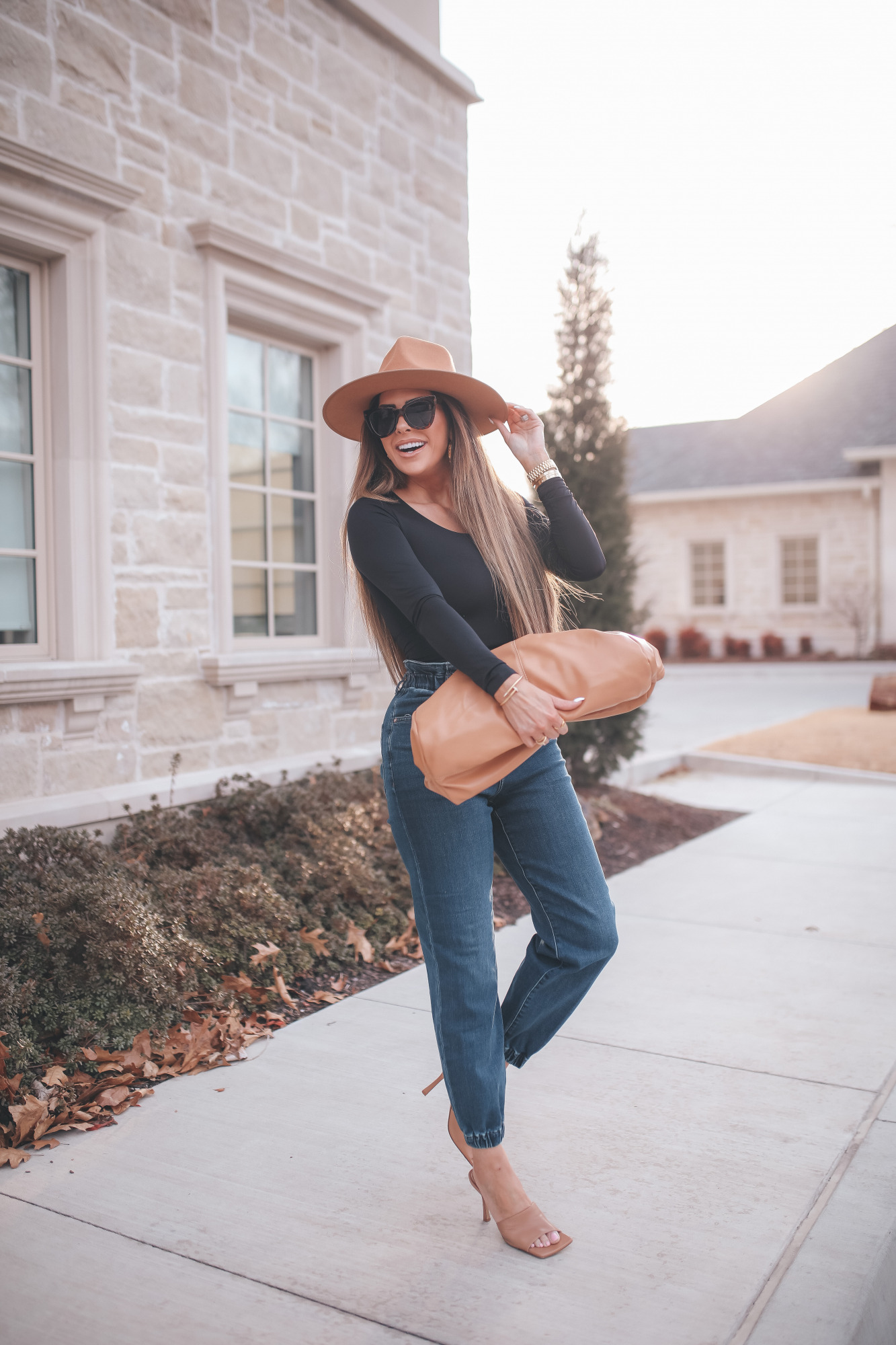 express spring fashion 2021, bottega clutch dupe, denim high waisted joggers, emily gemma15 |Body Contour by popular US fashion blog, The Sweetest Thing: image of a Emily Gemma wearing an Express black bodysuit, Express high waisted joggers, tan heel slide sandals, tan felt fedora, and holding a Bottega clutch dupe.