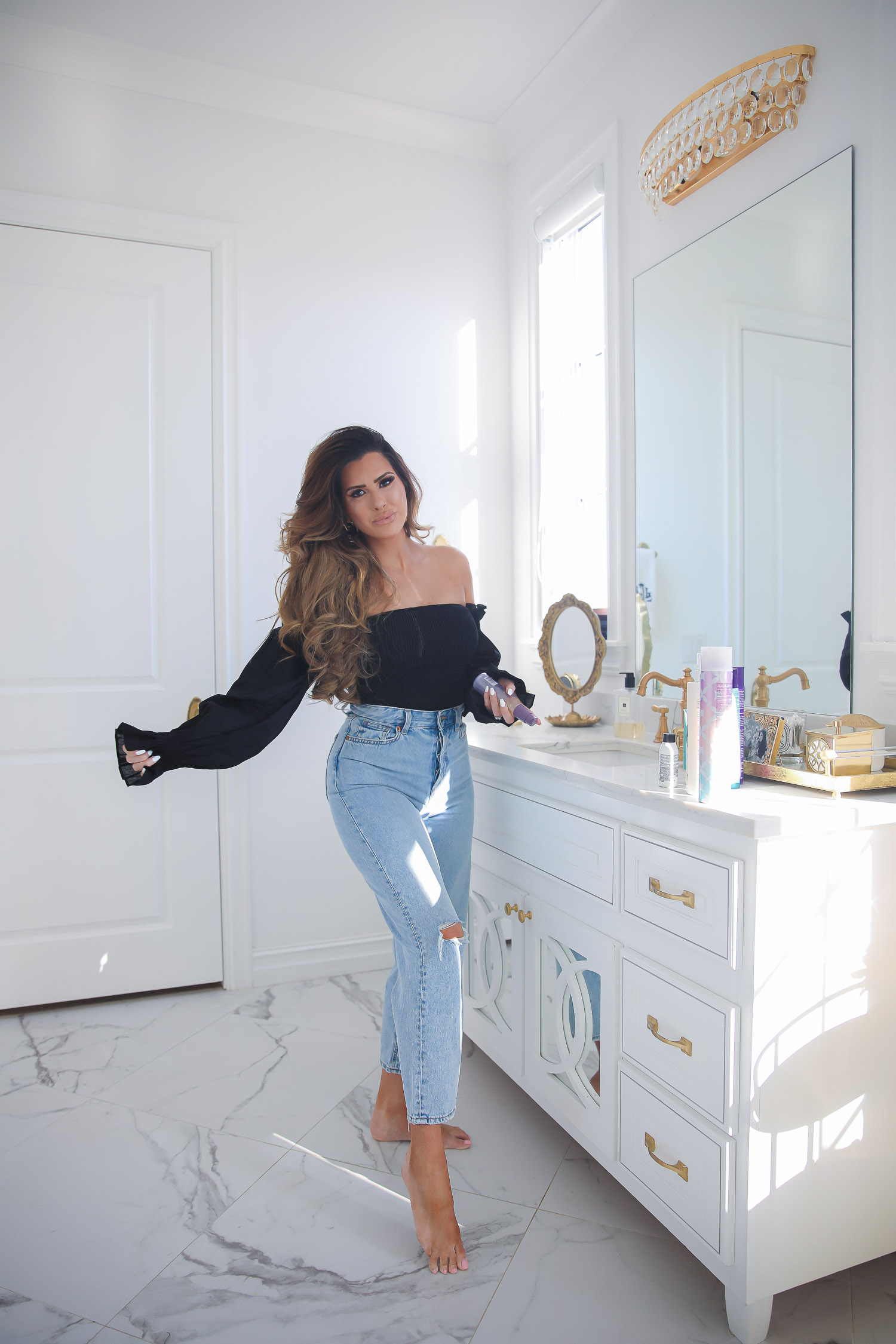 hair dot com, best hair products for long hair and extensions, Purology shampoo and conditioner, emily gemma, the sweetest thing blog |Hair Products by popular US beauty blog, The Sweetest Thing: image of Emily Gemma standing in her bathroom and wearing a black off the shoulder top, high waisted light denim jeans, and holding a bottle of Purology hair product in her hand. 