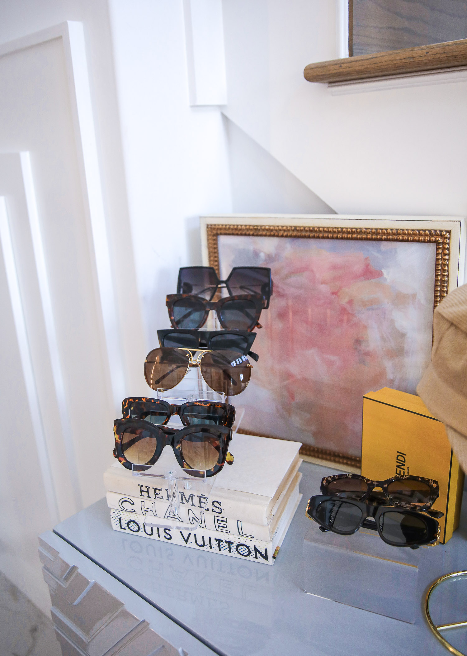Amazon home decor sunglasses display, acrylic sunglasses display, best amazon sunglasses summer 2021, Emily Gemma |Amazon Must Haves by popular US life and style blog, The Sweetest Thing: image of a orange Hermes tray filled with gold earring stands, Louis Vuitton jewelry, and a glass dish filled with mints, sunglasses on an acrylic sunglasses stand, and Christian Dior hat on a gold hat stand. 
