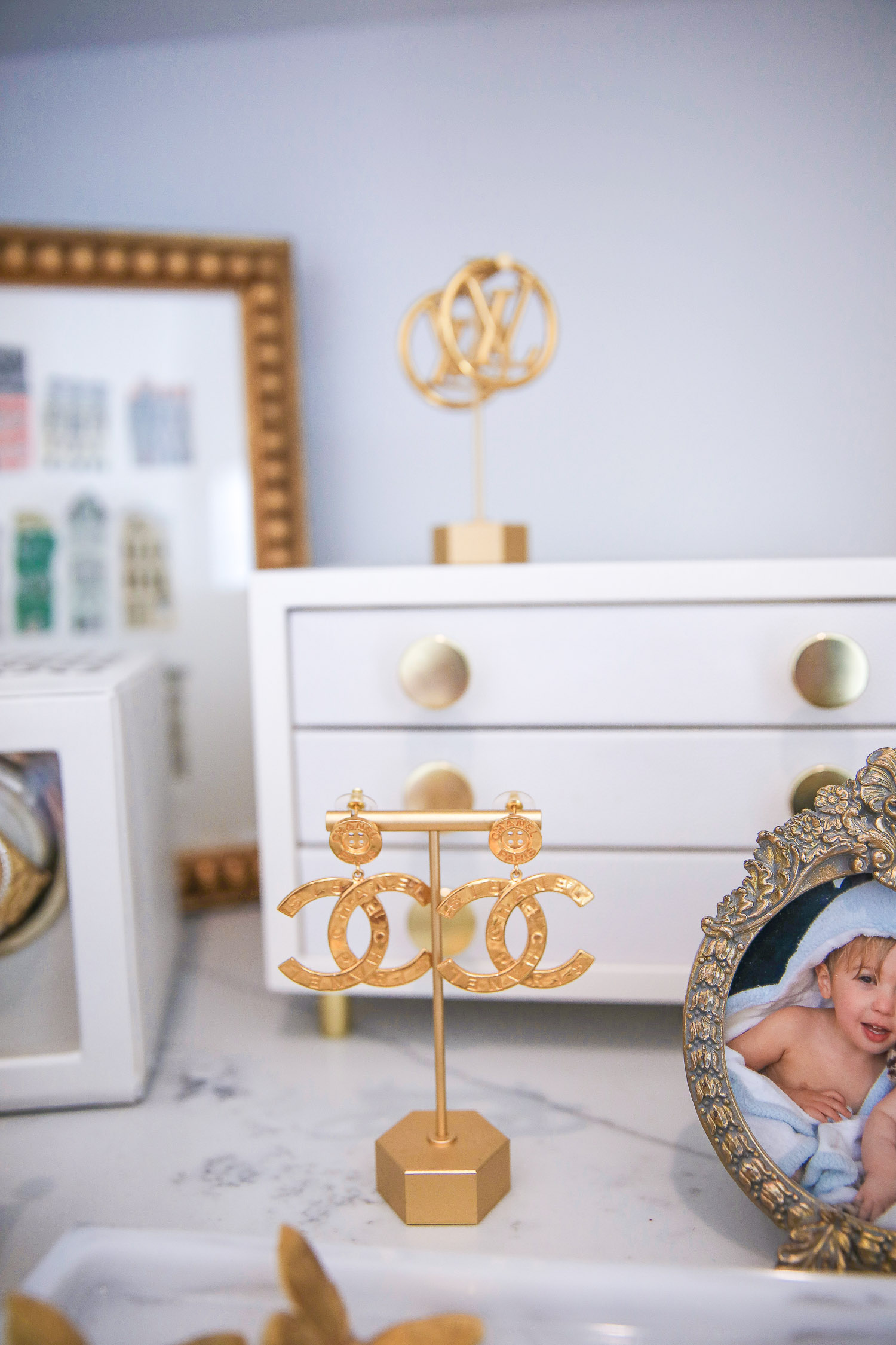 Amazon must haves jewelry holder, gold earring stands amazon, Emily Gemma amazon store, Chanel gold button earrings spring 2021, designer jewelry collection |Amazon Must Haves by popular US life and style blog, The Sweetest Thing: image of gold picture frames, gold jewelry holders, white jewelry box, pink velvet bracelet cushion, Chanel Gold button collection earrings on a gold earring stand, and gold necklace holder on a white marble counter top. 