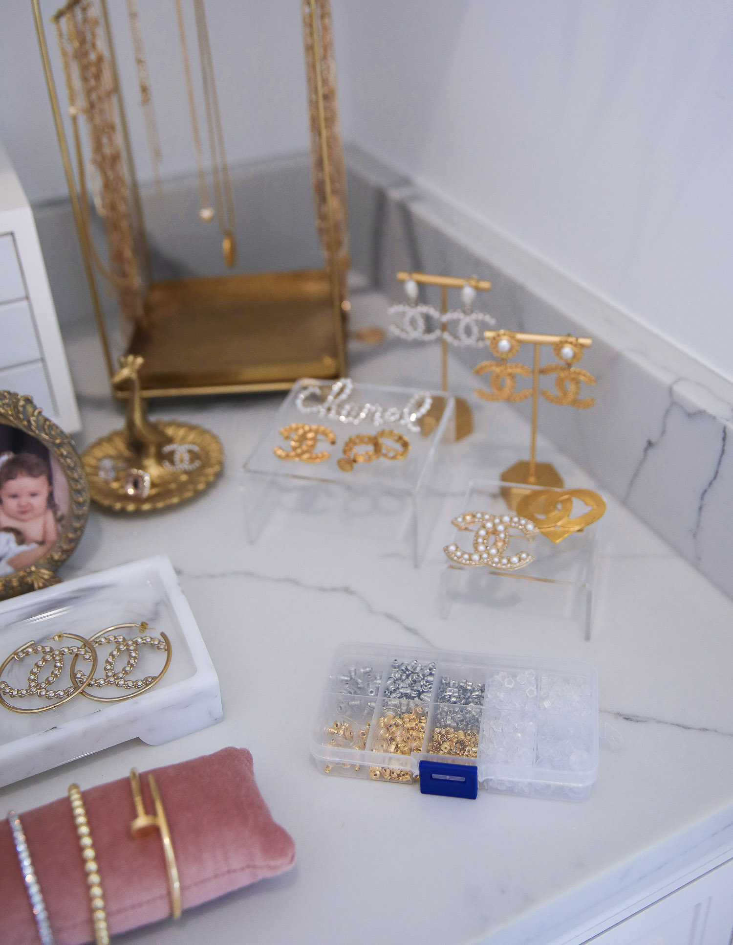 amazon earring backs, Chanel earrings 2021, amazon must haves Emily Gemma |Amazon Must Haves by popular US life and style blog, The Sweetest Thing: image of gold picture frames, gold jewelry holders, white jewelry box, pink velvet bracelet cushion, earring backs in a storage container, and gold necklace holder on a white marble counter top. 