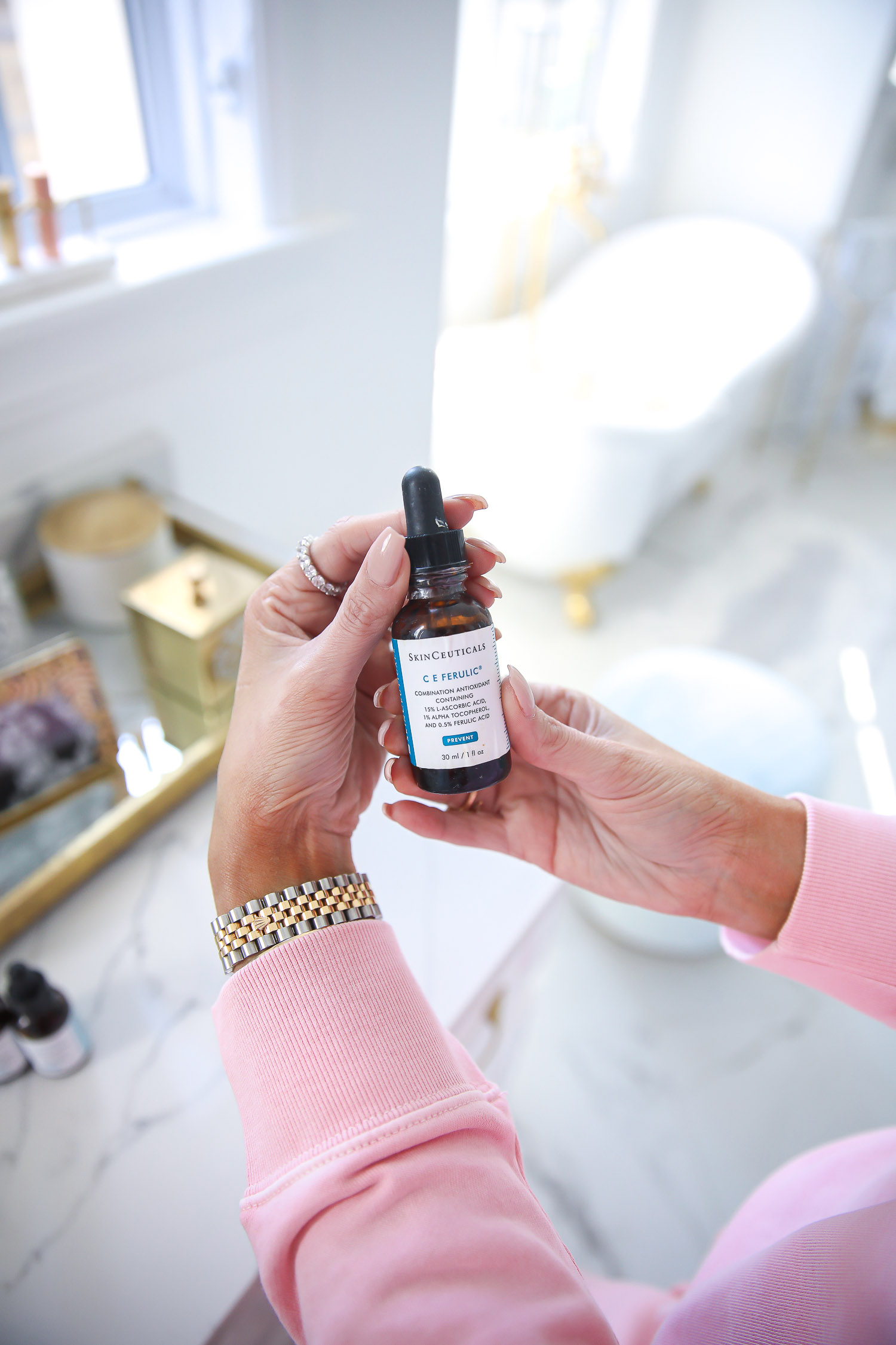 Skinceuticals CE Ferulic SilyMarin Phloretin CF, best Vitamim C serum, CE Ferulic vs Phloretin CF, why do you need Vitamin C, emily gemma skincare |Vitamin C Skincare by popular beauty blog, The Sweetest Thing: image of Emily Gemma standing in her bathroom and wearing a pink sweatsuit while holding a bottle SkinCeuticals skin care product. 