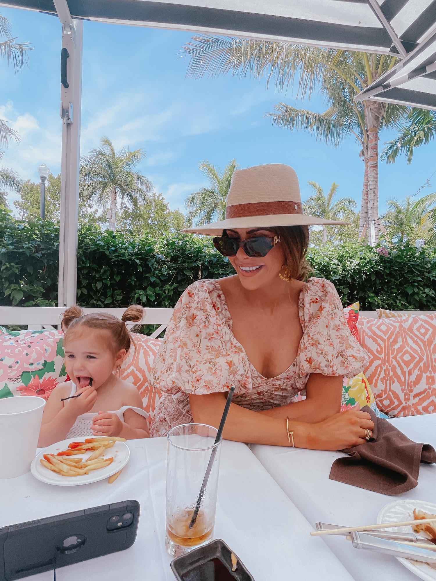 Palm beach white elephant lola41, cute outfit ideas palm beach, emily gemma, toddler fashion blog | Instagram Recap by popular US life and style blog, The Sweetest Thing: image of Emily Gemma and her daughter sitting at a table and wearing a brown fedora hat, sunglasses, cream floral print puff sleeve dress and white smock dress.
