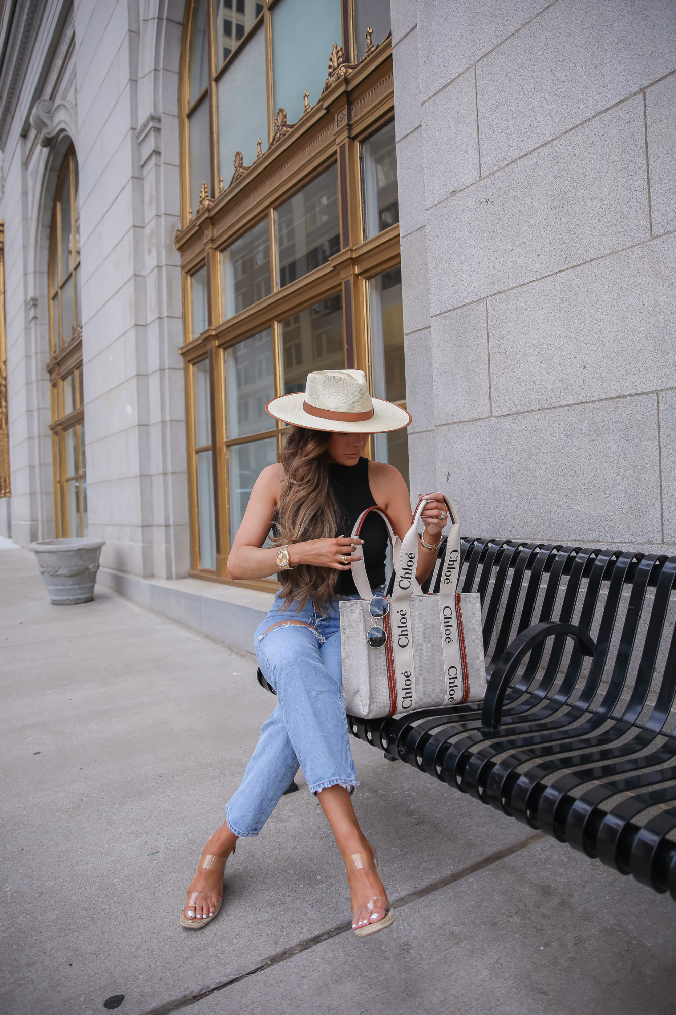 Summer Outfit by popular US fashion blog, The Sweetest Thing: image of Emily Gemma standing outside in front of a building with gold framed windows and wearing a cream fedora hat, BP mock neck tank, Agolde jeans, Steve Madden clear strap espadrilles, and holding a Chloe tote bag. 