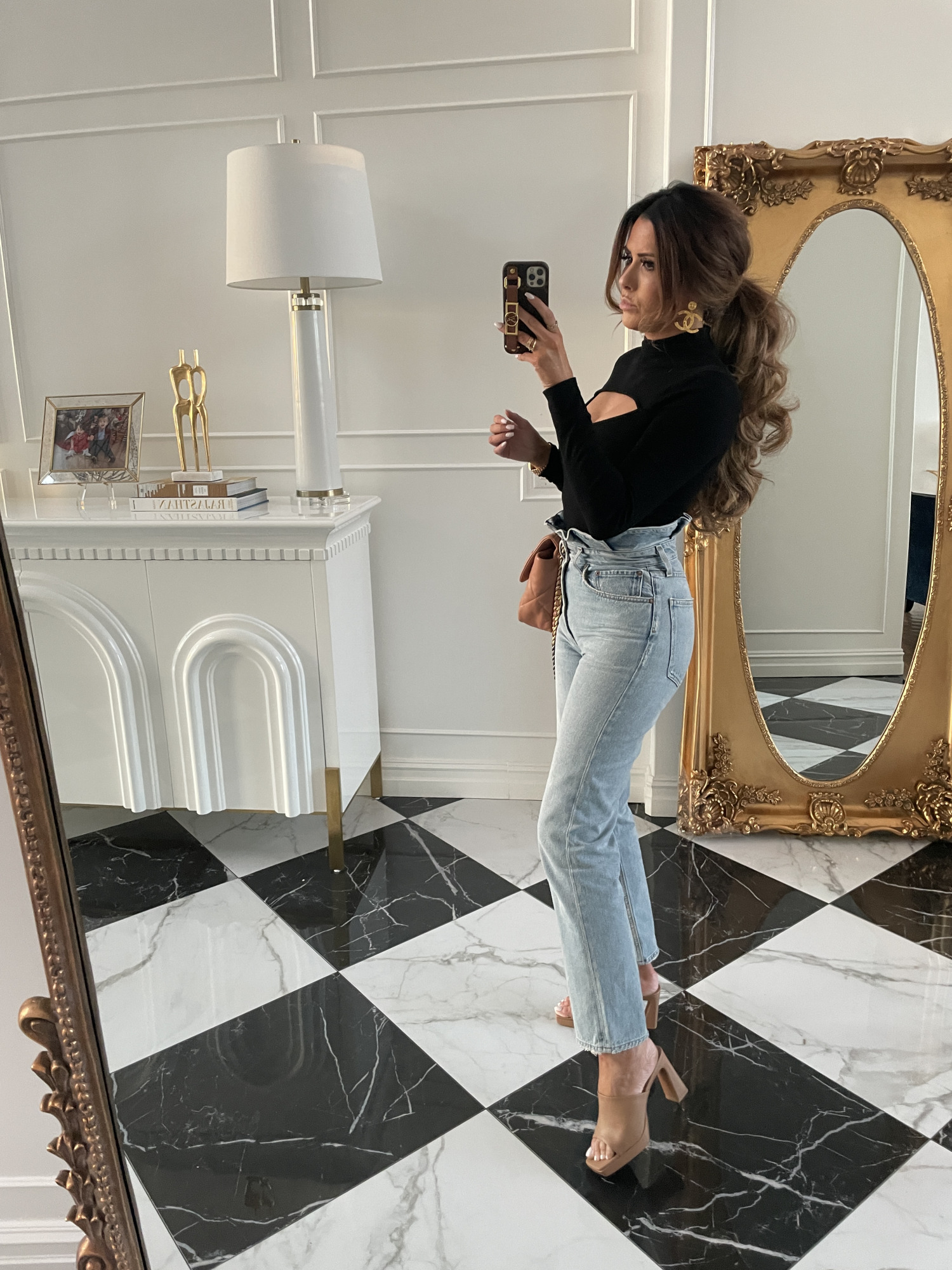 Instagram Recap by popular US life and style blog, The Sweetest Thing: image of Emily Gemma standing next to a gold full body mirror and wearing a black keyhole long sleeve top tan slide block heel mules, gold Chanel statement earrings, and light wash high waist jeans. 
