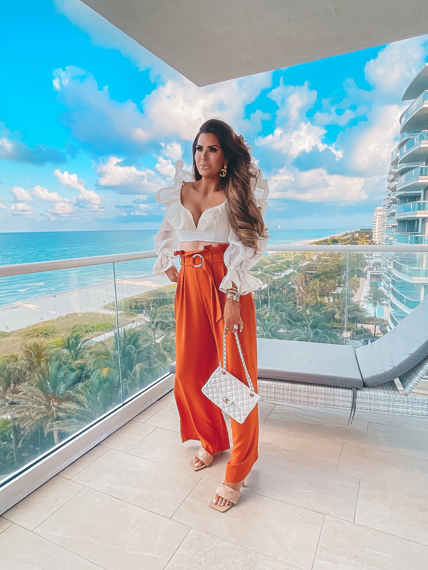 Zimmermann top, white long sleeve crop top, high waisted orange linen pants, amazon heels, bottega Veneta dupe heels, white chanel bag, Emily Ann gemma | Instagram Recap by popular US life and style blog, The Sweetest Thing: image of Emily Gemma wearing a cream long sleeve crop top with orange wide leg high waist pants, tan braided strap sandals, gold jewelry and holding a white quilted designer handbag. 