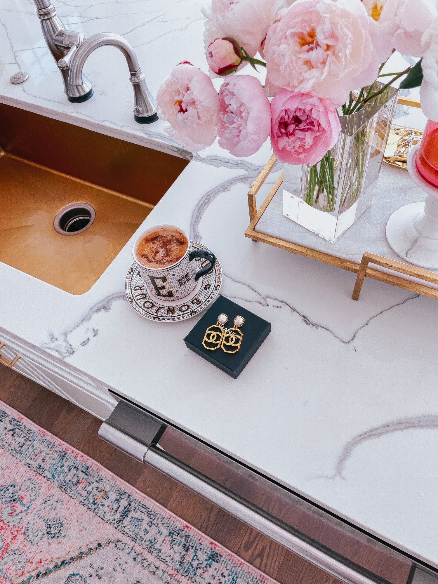 Emily-ann-gemma-kitchen-details-kitchen-decor-chanel-earrings-pretty-coffee-cup-peonies | Instagram Recap by popular US life and style blog, The Sweetest Thing: image of a black and white monogram Anthropologie mug and saucers next to a box of gold Chanel statement earrings a rose gold and white marble tray holding a clear glass vase filled with pink peonies. 