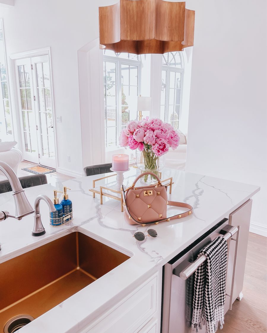 Spring Kitchen by popular US life and style blog: image of a kitchen with white cabinets, wood flooring, wooden light pendants, marble counter tops, and light pink and blue runner rug. 