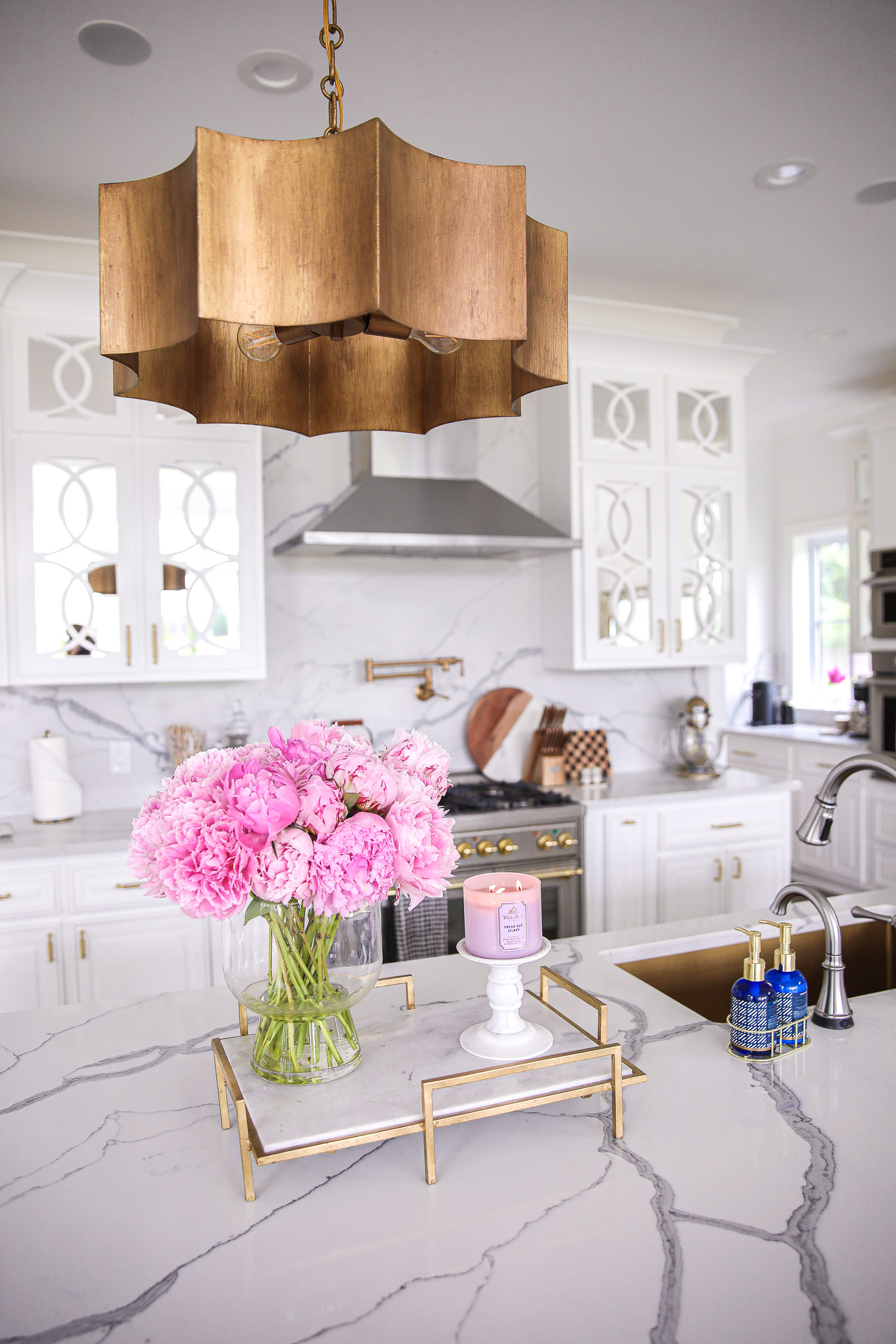 Pinterest white kitchen quartz, ilv majestic stove, Emily Gemma kitchen, gold kitchen sink, Emily Gemma kitchen, grey and gold barstools | Spring Kitchen by popular US life and style blog: image of a kitchen with white cabinets, wood flooring, wooden light pendants, marble counter tops, and light pink and blue runner rug. 
