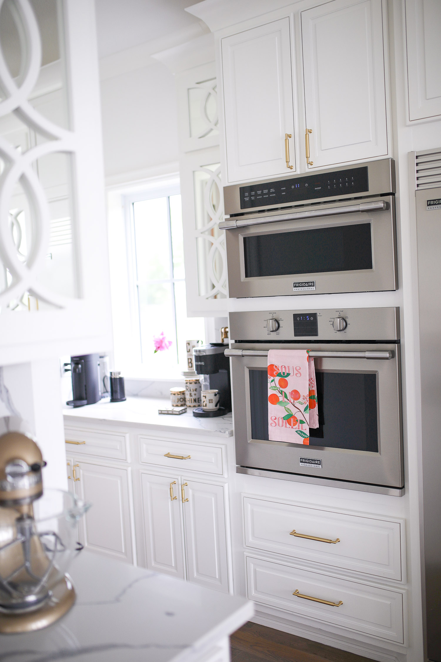 Pinterest white kitchen quartz, ilv majestic stove, Emily Gemma kitchen, gold kitchen sink, Emily Gemma kitchen, grey and gold barstools | Spring Kitchen by popular US life and style blog: image of a kitchen with white cabinets, wood flooring, wooden light pendants, marble counter tops, pink citrus print Sous dishtowel, and light pink and blue runner rug. 