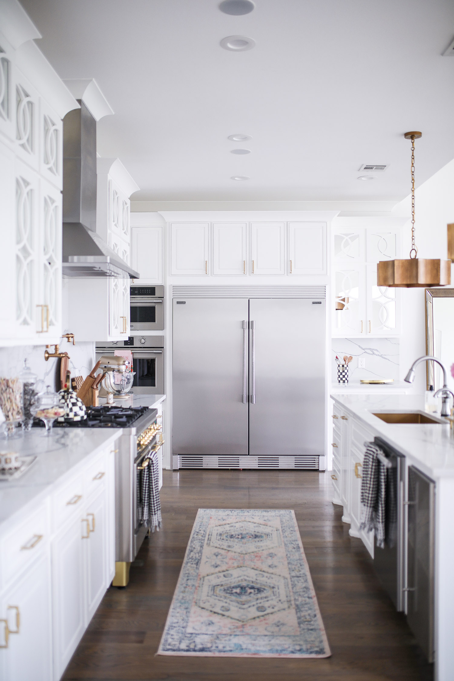 Spring Kitchen by popular US life and style blog: image of a kitchen with white cabinets, wood flooring, wooden light pendants, marble counter tops, and light pink and blue runner rug. 