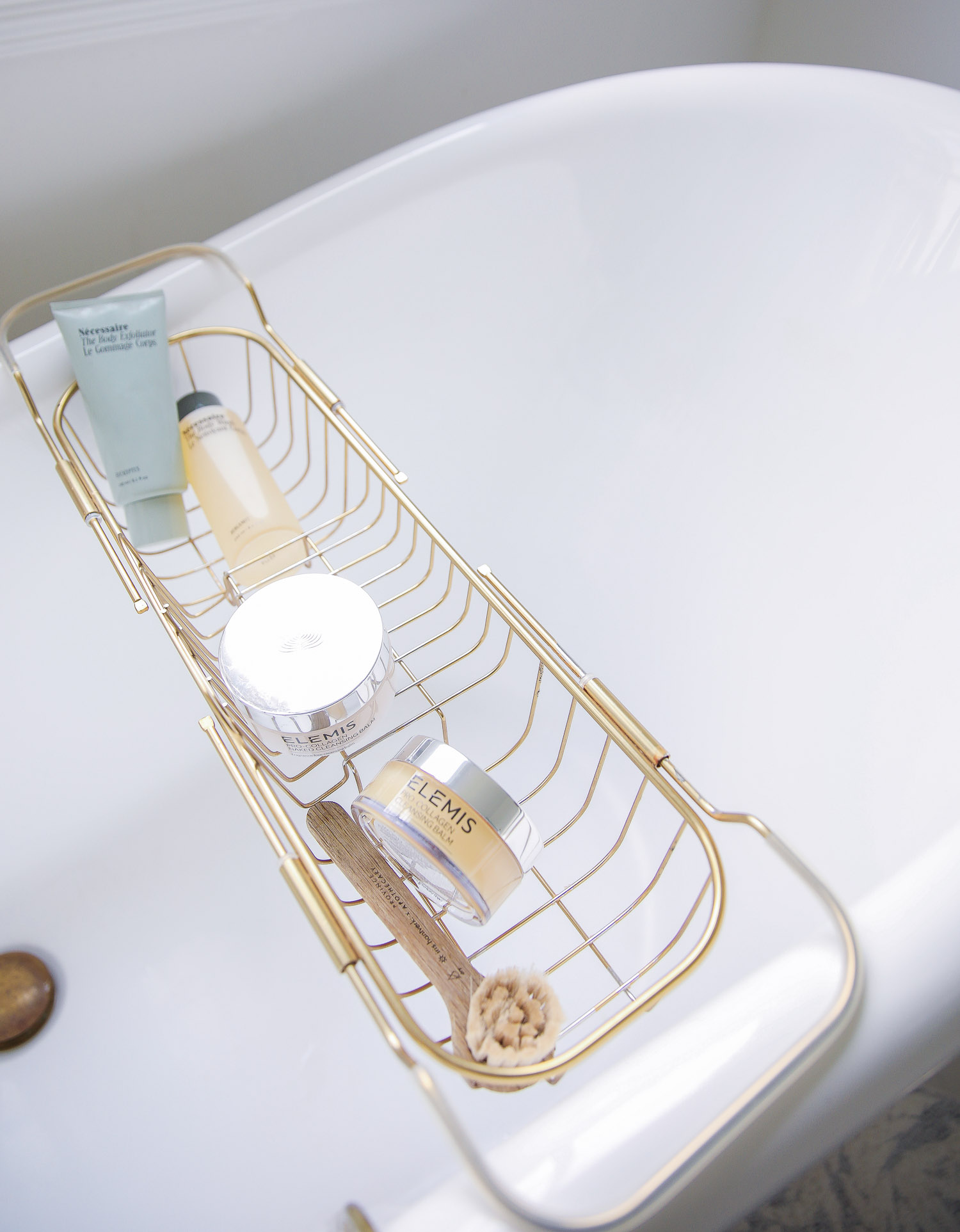 Elemis cleansing balm Nordstrom sale 2021, Emily gemma master bathroom, Nordstrom anniversary sale 2021 beauty must haves, anthropologie bathrom decor 2021, pinterest bathroom all white gold | Nordstrom Anniversary Sale 2021 by popular US life and style blog, The Sweetest Thing: image of a gold wire bathtub tray on a white clawfoot tub filled with Elemis skincare products and a wood handle scrub brush. 