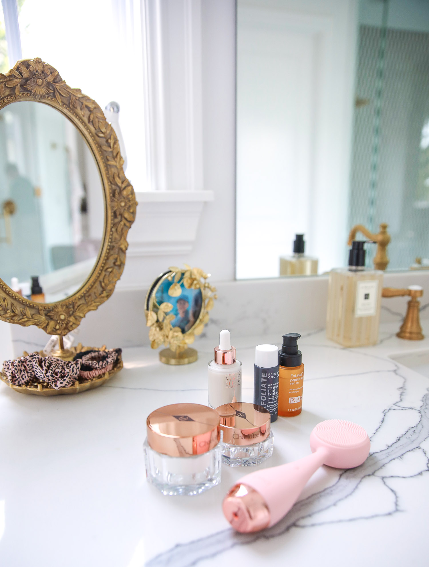 Emily gemma master bathroom, Nordstrom anniversary sale 2021 beauty must haves, anthropologie bathrom decor 2021, pinterest bathroom all white gold | Nordstrom Anniversary Sale 2021 by popular US life and style blog, The Sweetest Thing: image of a silicone face scrubber, gold filigree hand mirror, and skincare products on a white marble counter. 