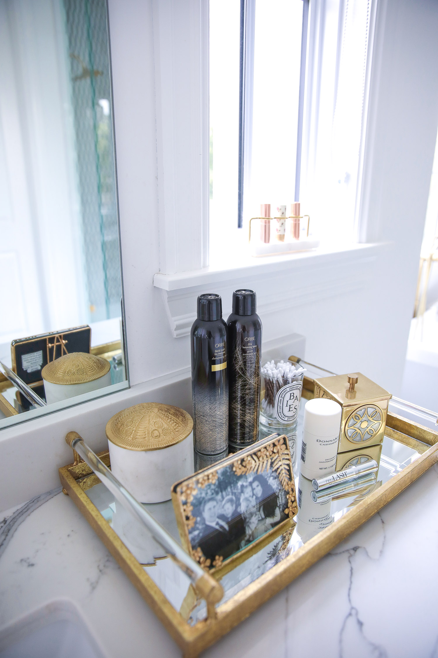 Anthropologie home decor summer 2021, oribe dry texture spray NSALE 20201 | Instagram Recap by popular US life and style blog, The Sweetest Thing: image of a gold mirrored tray filled with a gold picture frame, white votive candle, q-tip holder, and Oribe texturizing spray, resting on a bathroom vanity