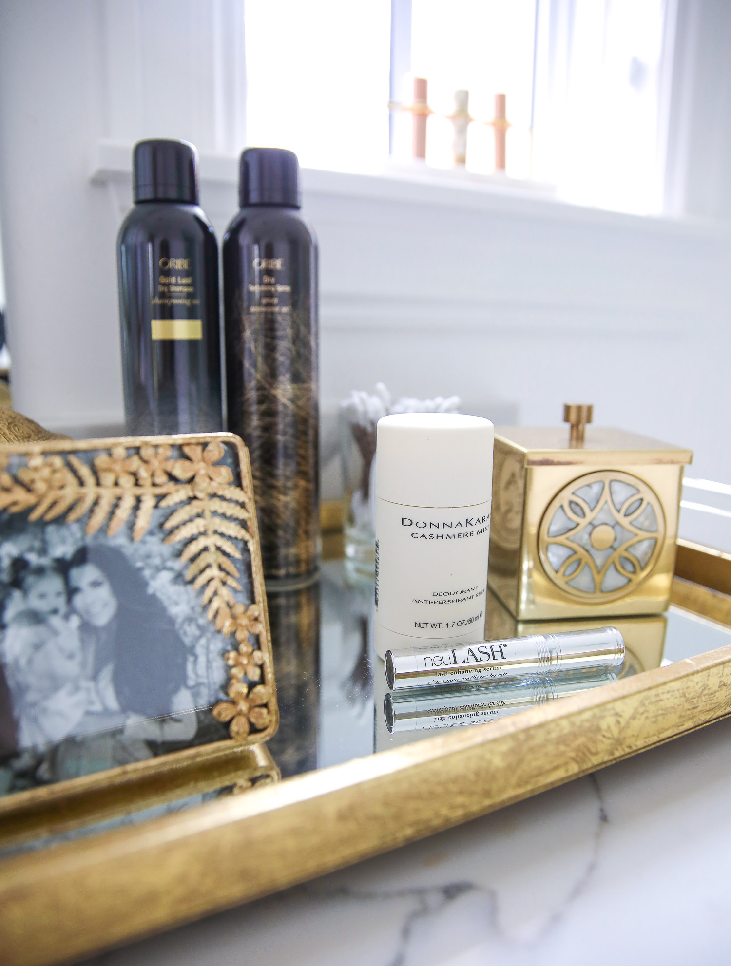 Emily gemma master bathroom, Nordstrom anniversary sale 2021 beauty must haves, anthropologie bathrom decor 2021, pinterest bathroom all white gold | Nordstrom Anniversary Sale 2021 by popular US life and style blog, The Sweetest Thing: image of a gold metal and mirrored tray with Oribe dry texture spray bottles, Donna Karan Cashmere beauty product, neu lash mascara, and gold picture frame with a black and white family photo. 