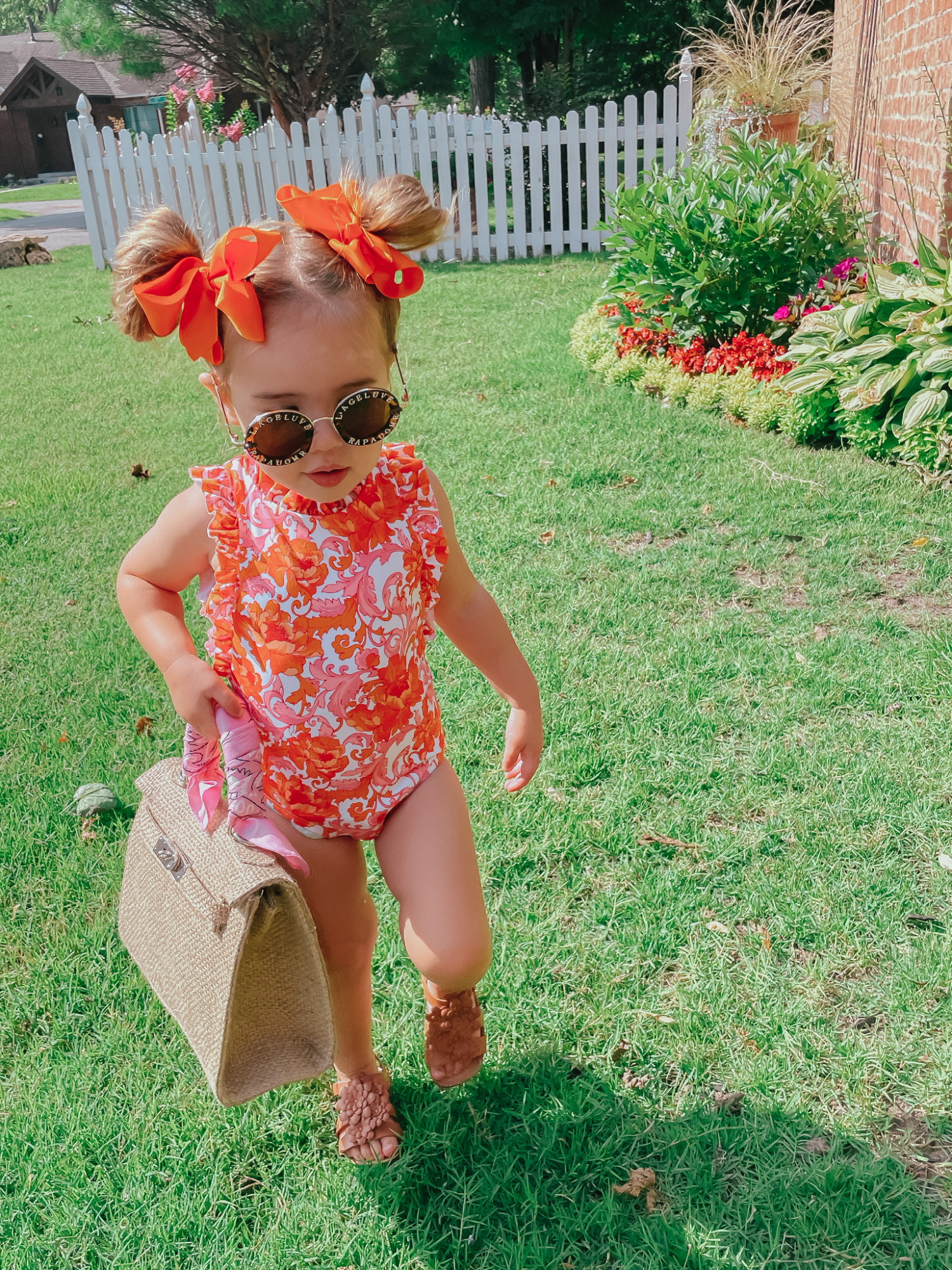 Sophia Gemma, Toddler Swimsuit, Toddler Bows, Swimwear for little girls, Kids Sunglasses, Baby Girl Summer Outfit Ideas | Instagram Recap by popular US life and style blog, The Sweetest Thing: image of a little girl wearing an orange and pink floral print Janie and Jack swimsuit, Zara sandals, orange hair bows, and holding a woven handbag. 