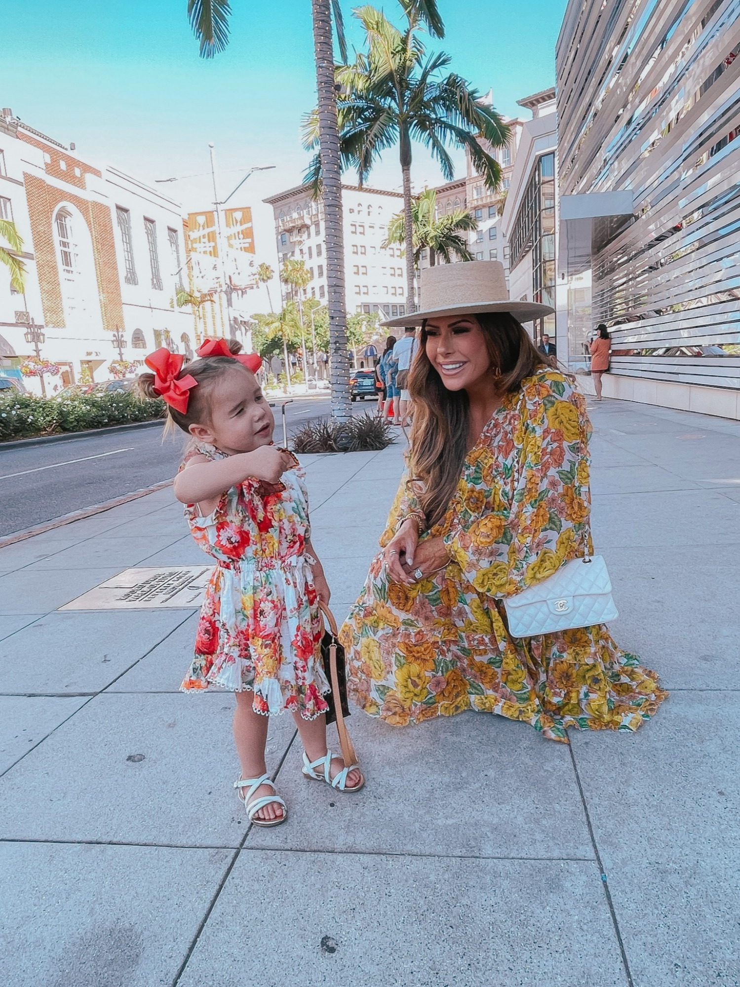 rodeo drive, mommy daughter shopping trip, Beverly Hills, Zimmermann dress, Zimmermann kids, Zimmermann mommy and daughter matching outfits, Chanel handbag, comfortable wedge sandals | Instagram Recap by popular US life and style blog, The Sweetest Thing: image of Emily Gemma wearing a floral print mini dress, Lack of Color boater hat, and white quilted Chanel purse and standing outside with her daughter Sophie wearing a floral print dress, white strap sandals, and red hair bows.