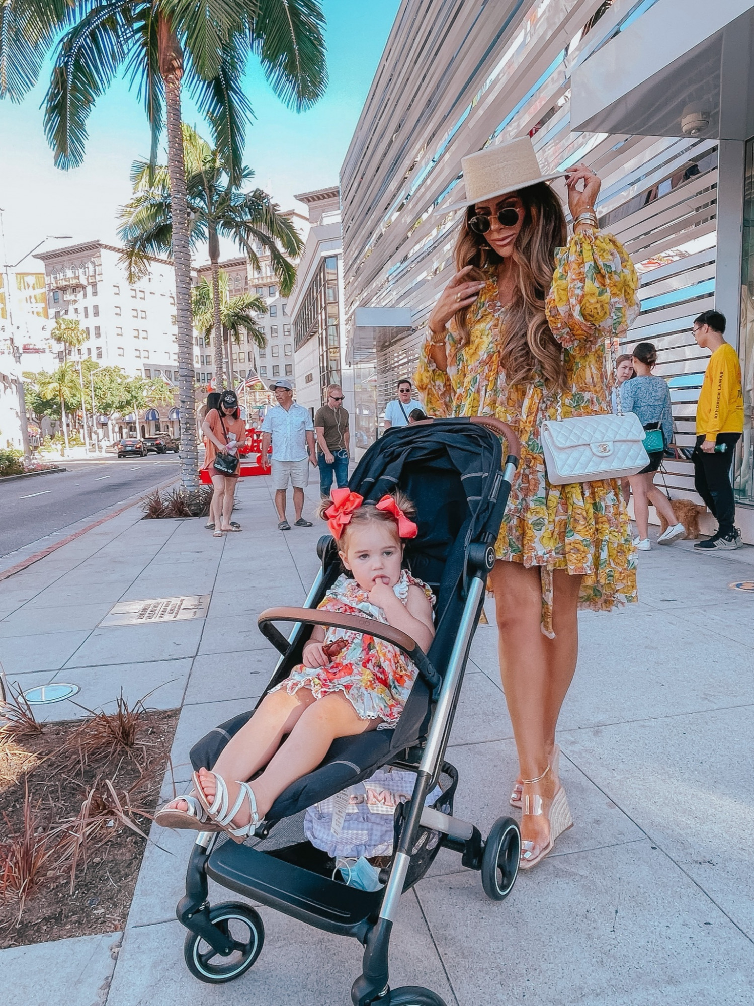  Instagram Recap by popular US life and style blog, The Sweetest Thing: image of Emily Gemma wearing a floral print mini dress, Lack of Color boater hat, and white quilted Chanel purse and standing outside with her daughter Sophie wearing a floral print dress, white strap sandals, and red hair bows.