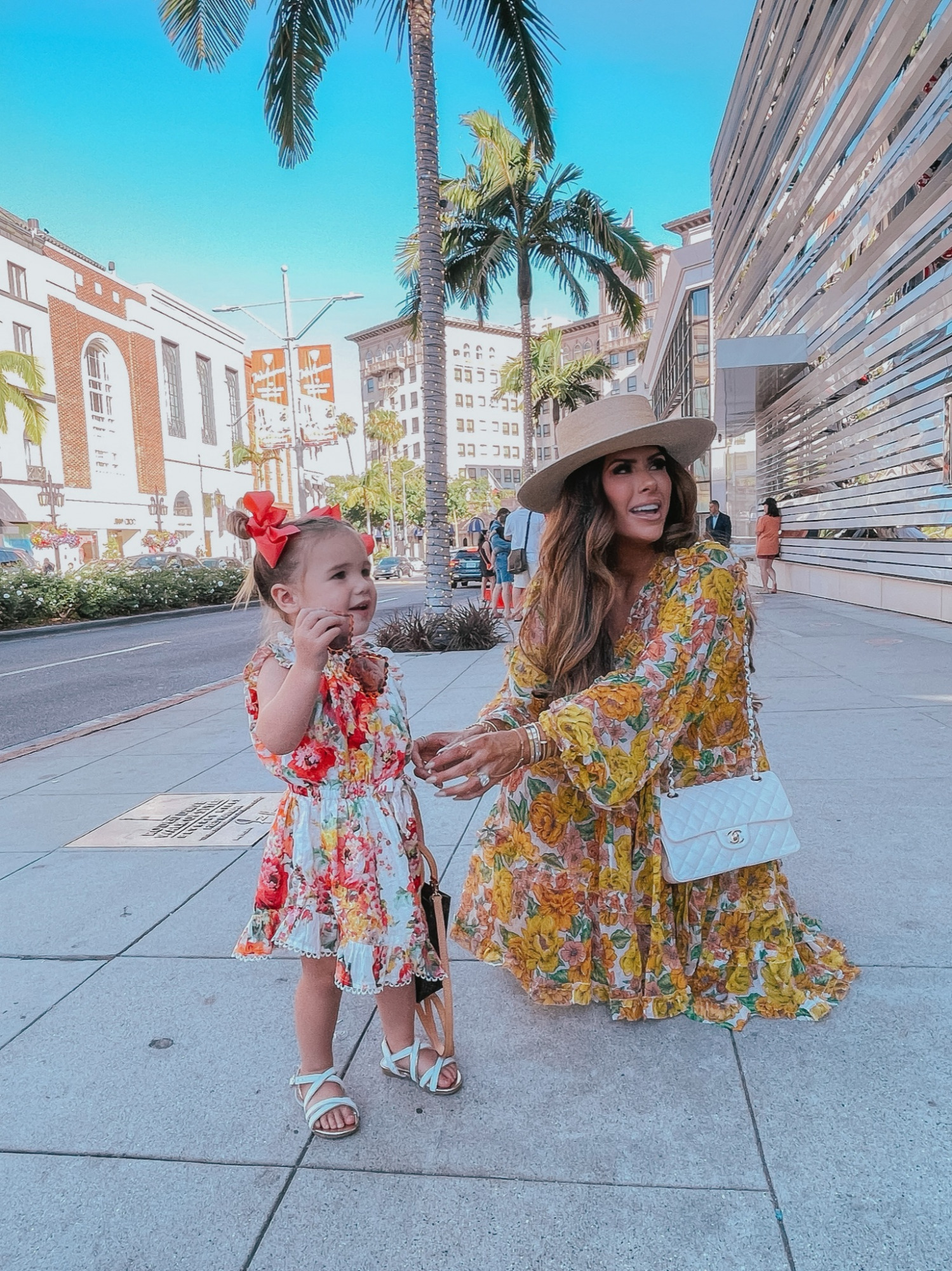  Instagram Recap by popular US life and style blog, The Sweetest Thing: image of Emily Gemma wearing a floral print mini dress, Lack of Color boater hat, and white quilted Chanel purse and standing outside with her daughter Sophie wearing a floral print dress, white strap sandals, and red hair bows.