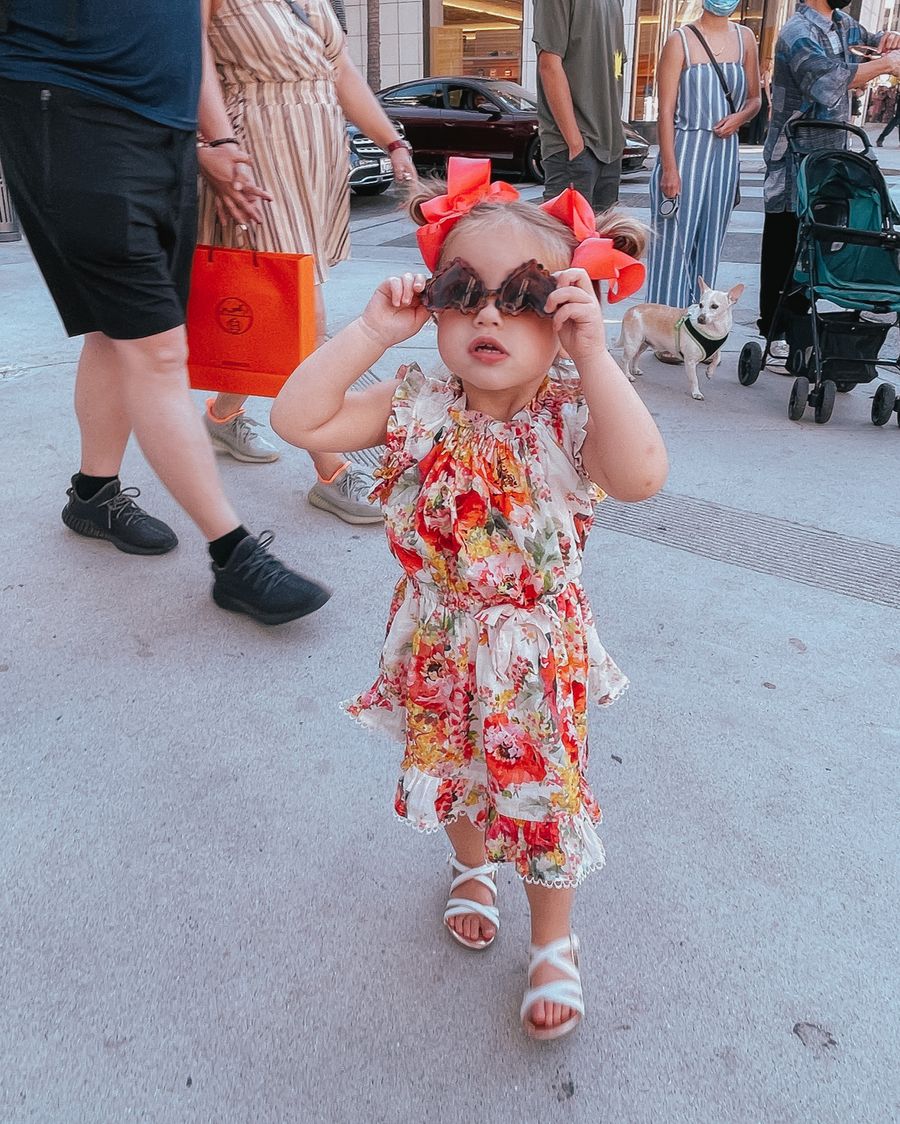 Sophia Gemma, Zimmermann Kids, Floral Dress for Little Girls, Bows for Little Girls, Kids Sunglasses | Instagram Recap by popular US life and style blog, The Sweetest Thing: image of a young girl wearing red hair bows, a floral print dress, heart frame sunglasses, and white strap sandals. 