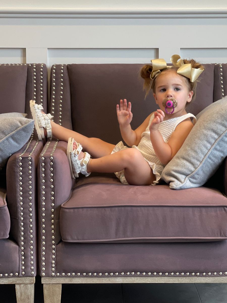 Little girls fashion, Sophia gemma, toddler style, toddler fashion, toddler girl fashion |  Instagram Recap by popular US life and style blog, The Sweetest Thing: image of a little girl sitting in a armchair and wearing gold bows, cream color sleeveless romper, and silver sandals. 